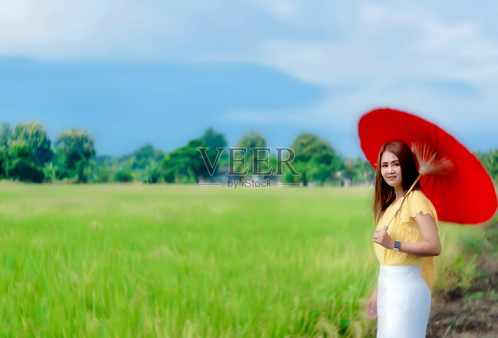 亚洲女性撑着红伞在草地上放松和享受。穿黄色衣服的漂亮女孩。去地球上干净的地方旅行，发现大自然的美。照片摄影图片