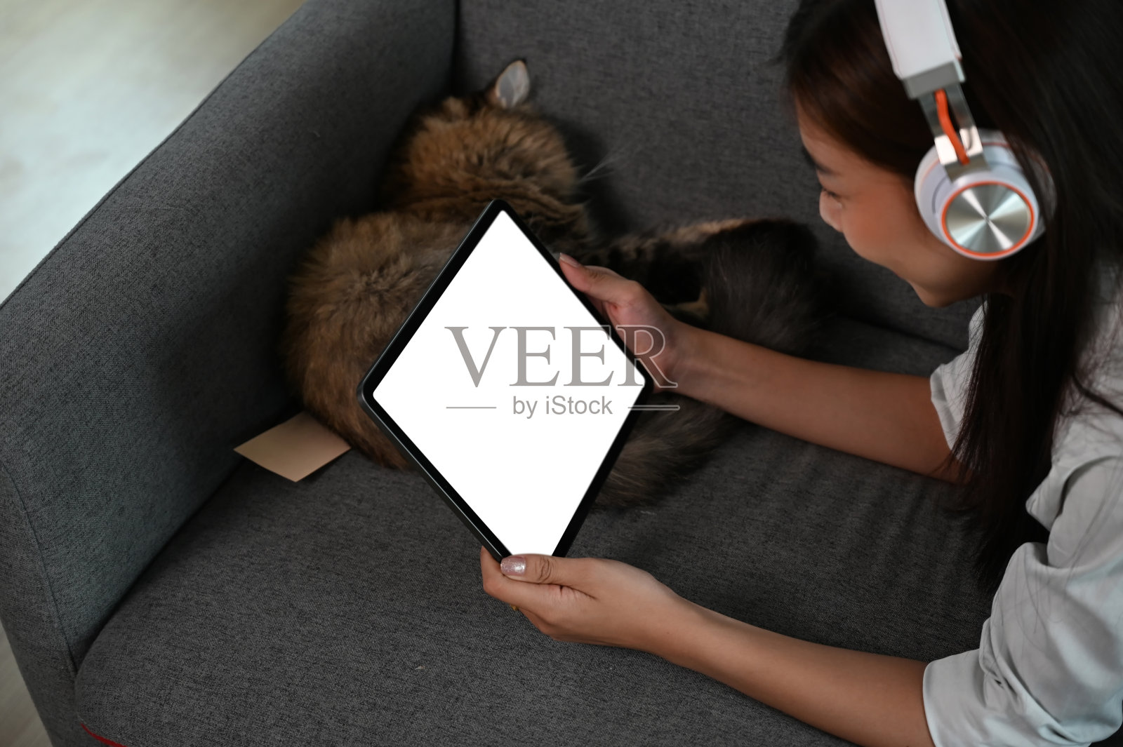 一个微笑的年轻女子坐在沙发上，戴着耳机在客厅的平板电脑上看东西。照片摄影图片