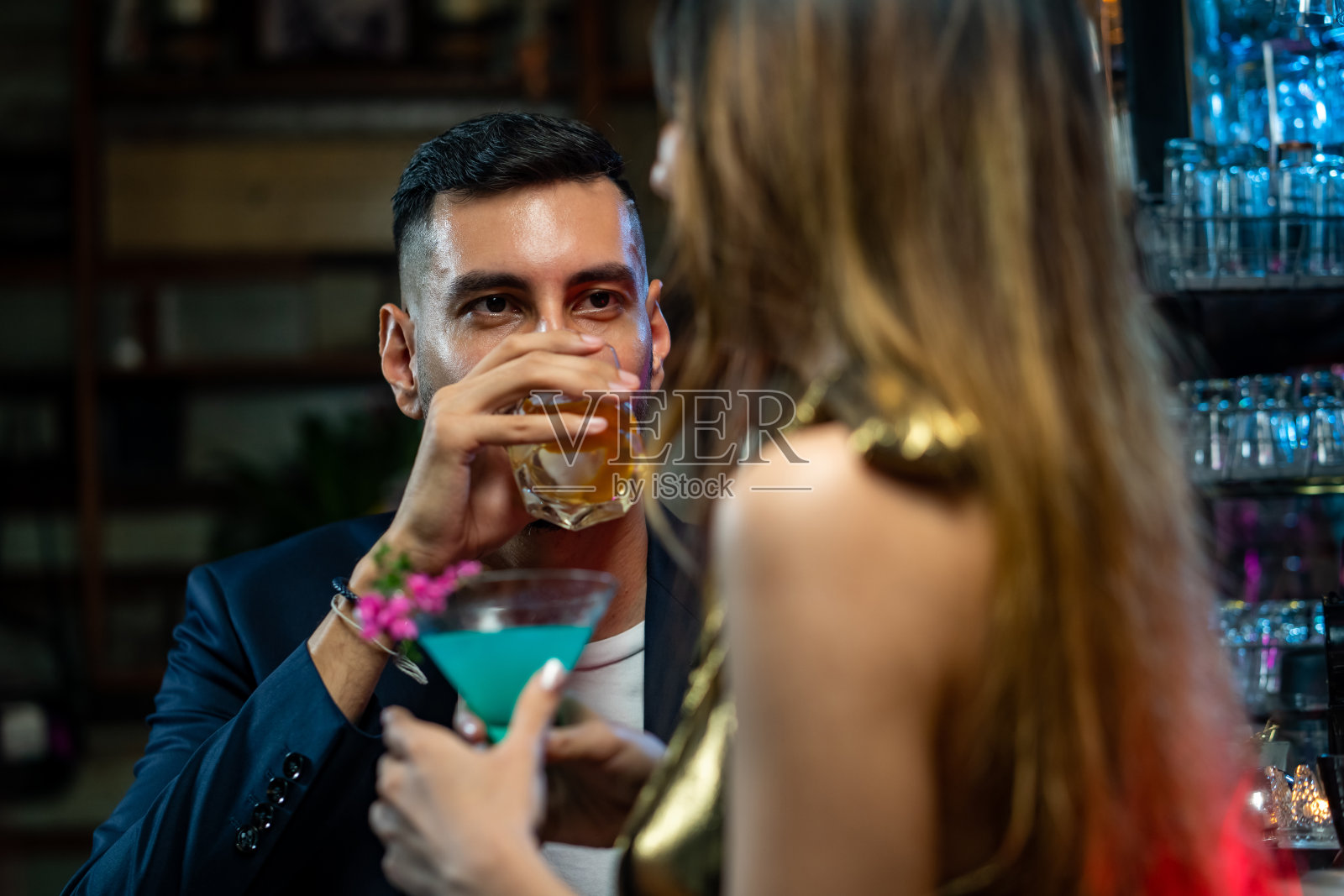 英俊的白人男子站在酒吧柜台调情，与美丽的女人聊天，享受酒精鸡尾酒在夜总会聚会。微笑的情侣在酒吧享受浪漫的约会。照片摄影图片