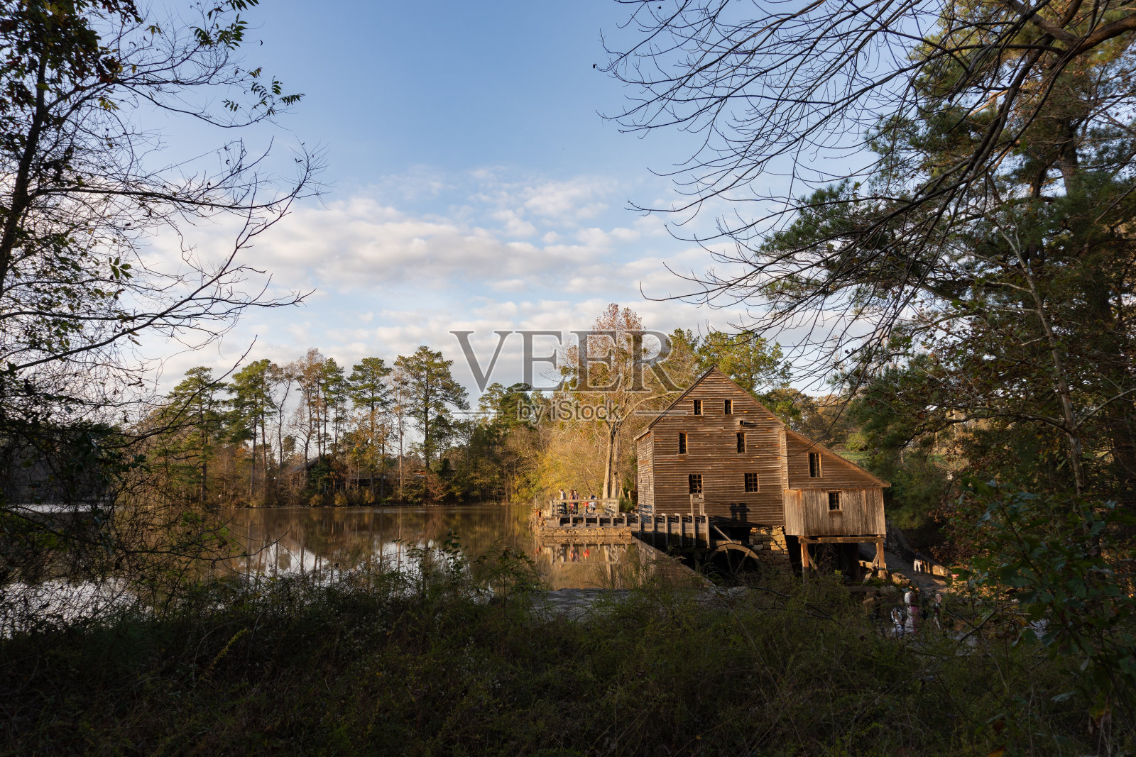 在北卡罗莱纳州历史悠久的耶茨米尔县公园的一个水池前的木结构建筑和水车的侧视图在秋天日落时;具有里程碑意义的照片摄影图片