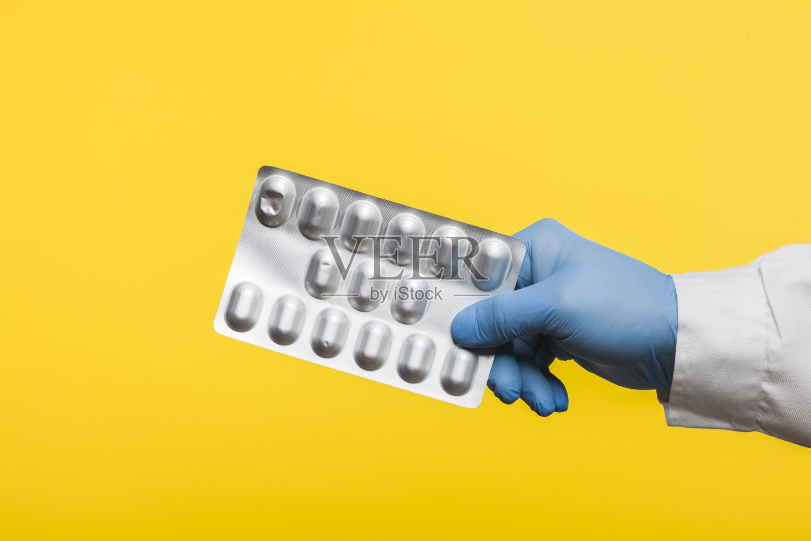 一名戴着防护手套的医生拿着一包COVID-19 SARS-CoV-2冠状病毒药片，在黄色背景上分离照片摄影图片