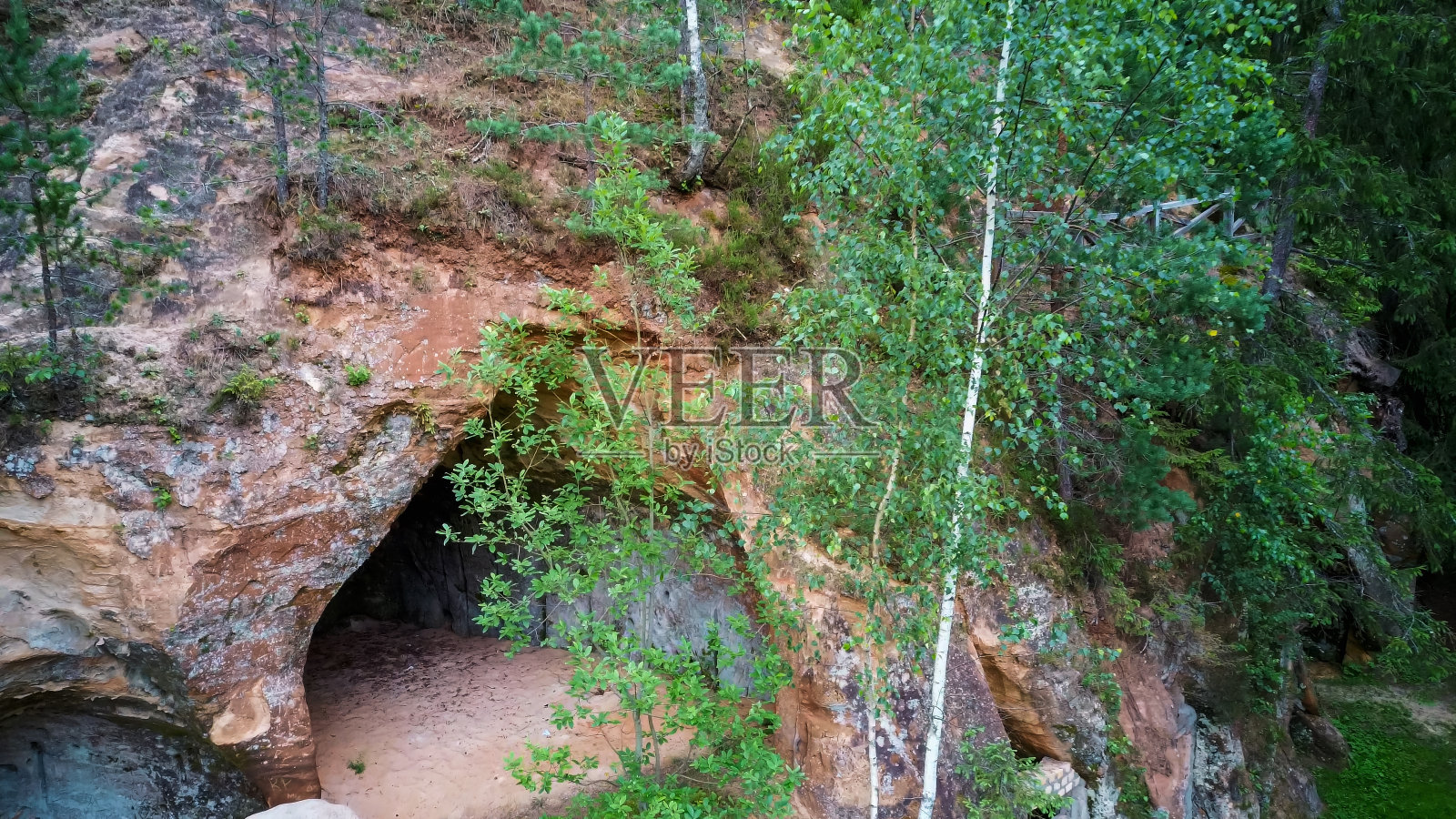 拉脱维亚Ligatne的砂岩洞穴。观赏洞穴岩石Lustuzis (Lustzis)在河岸的Ligatne河。带有旧木门的洞穴。照片摄影图片