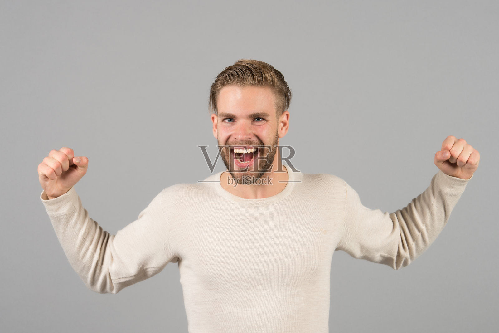 留胡子的男人，以胜利者的姿态。满脸胡子的快乐男人，脸上挂着微笑。穿着休闲t恤的金发时尚模特。胜利与成功理念照片摄影图片