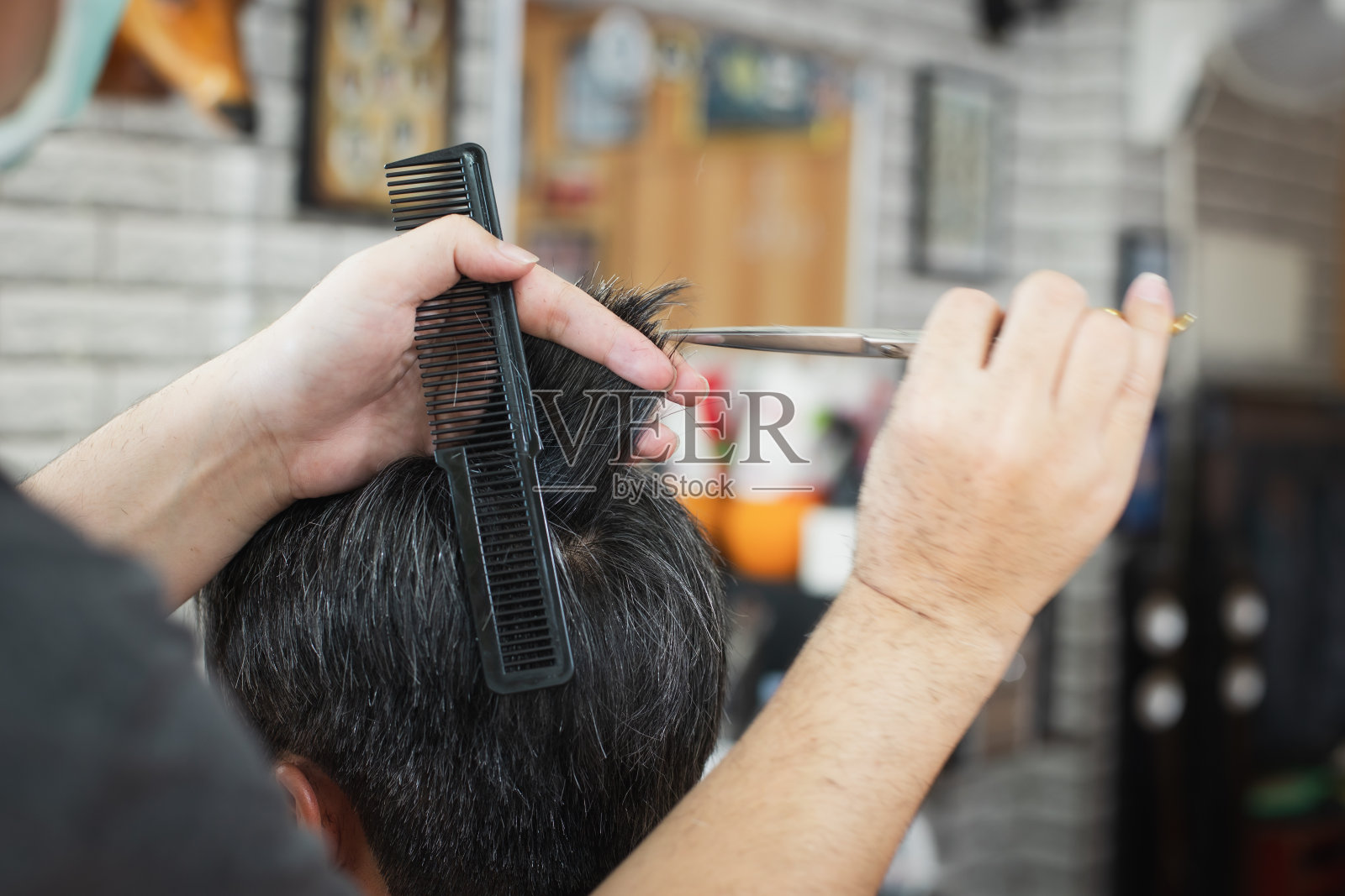 一名亚洲年轻人正在理发店里被专业理发师剪着。照片摄影图片