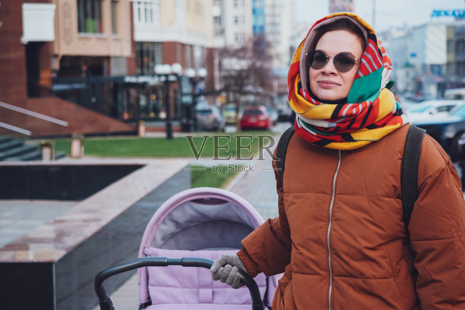 秋天，时髦的现代妈妈推着婴儿车在城市里散步。妈妈推着婴儿车穿过街道，特写镜头照片摄影图片