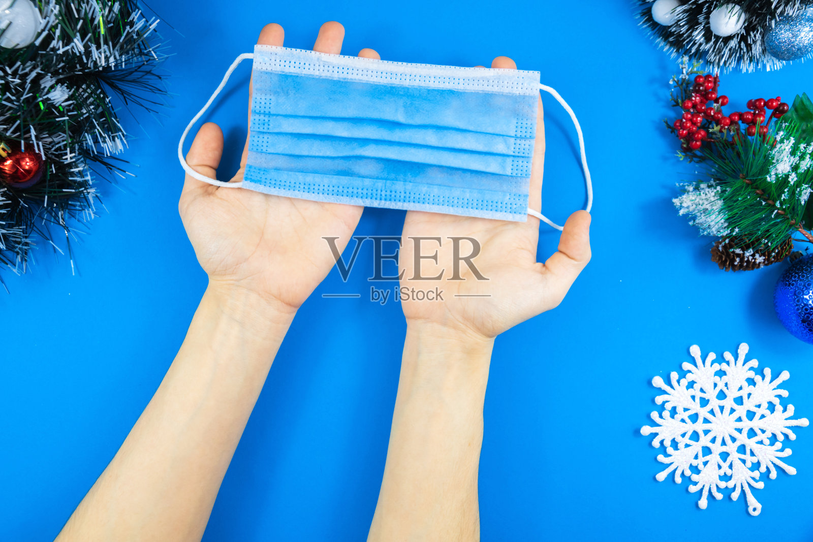 一个悲伤的男孩拿着一个面具对抗冠状病毒在蓝色背景和圣诞装饰照片摄影图片