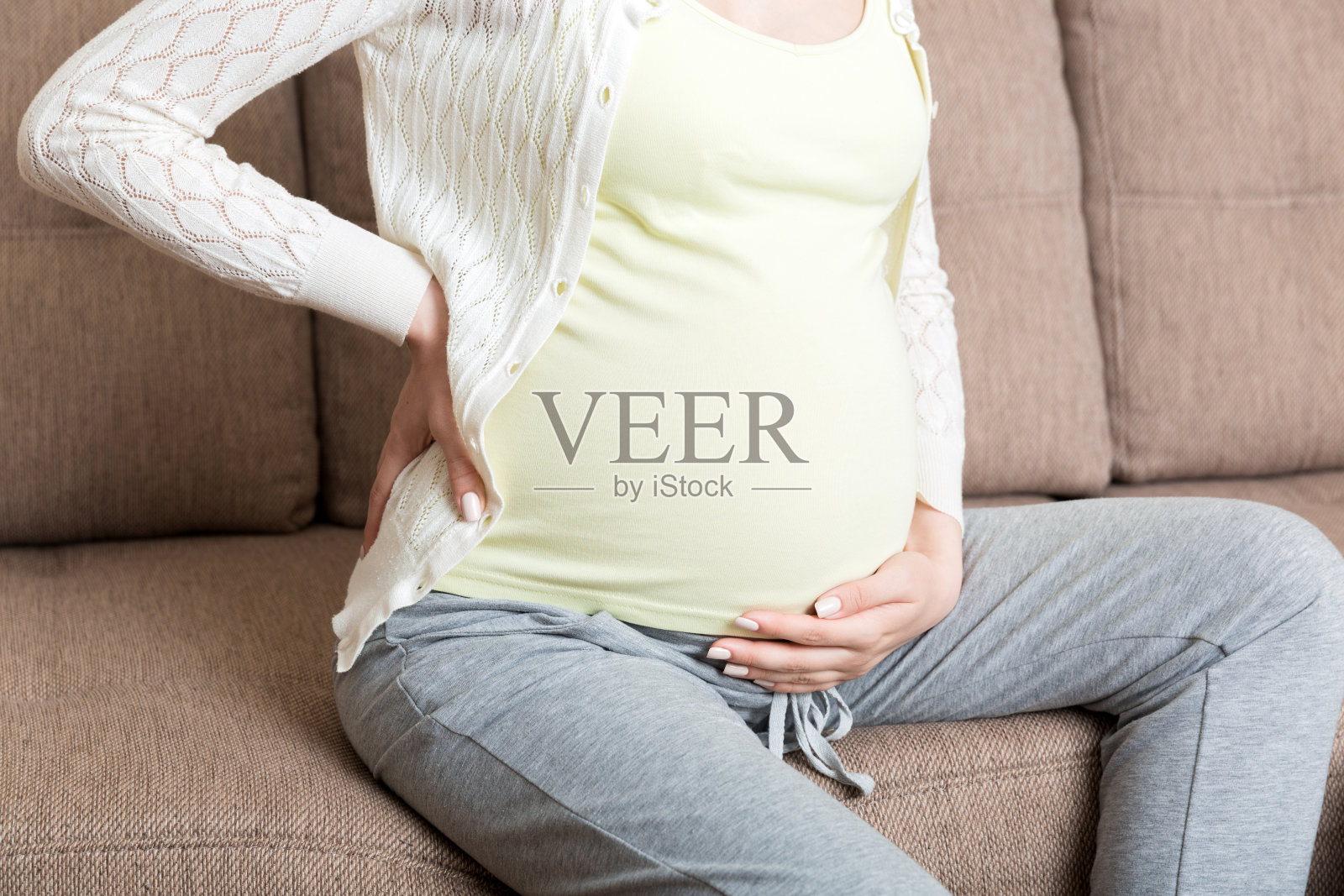 美丽的孕妇触摸她的肚子，并保持一只手在她的背部在家里的沙发上照片摄影图片