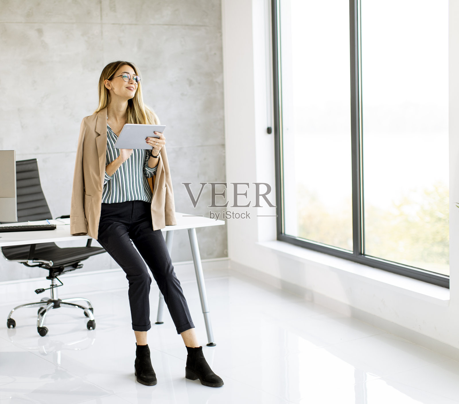 年轻的商业女性拿着平板电脑站在现代办公室里照片摄影图片