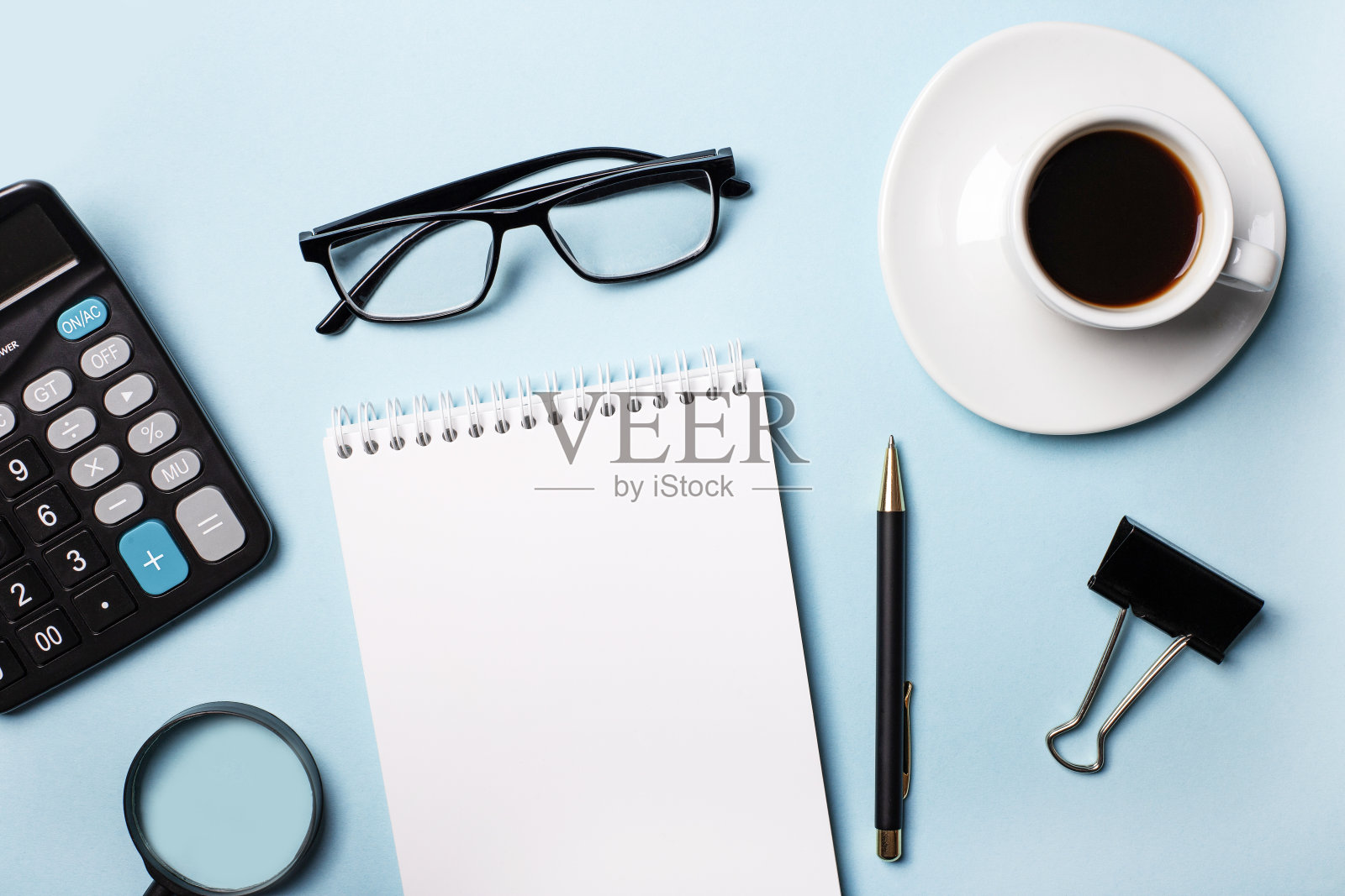 计算器，空白笔记本，钢笔，咖啡杯，放大镜和浅蓝色背景上的眼镜。俯视图特写照片摄影图片