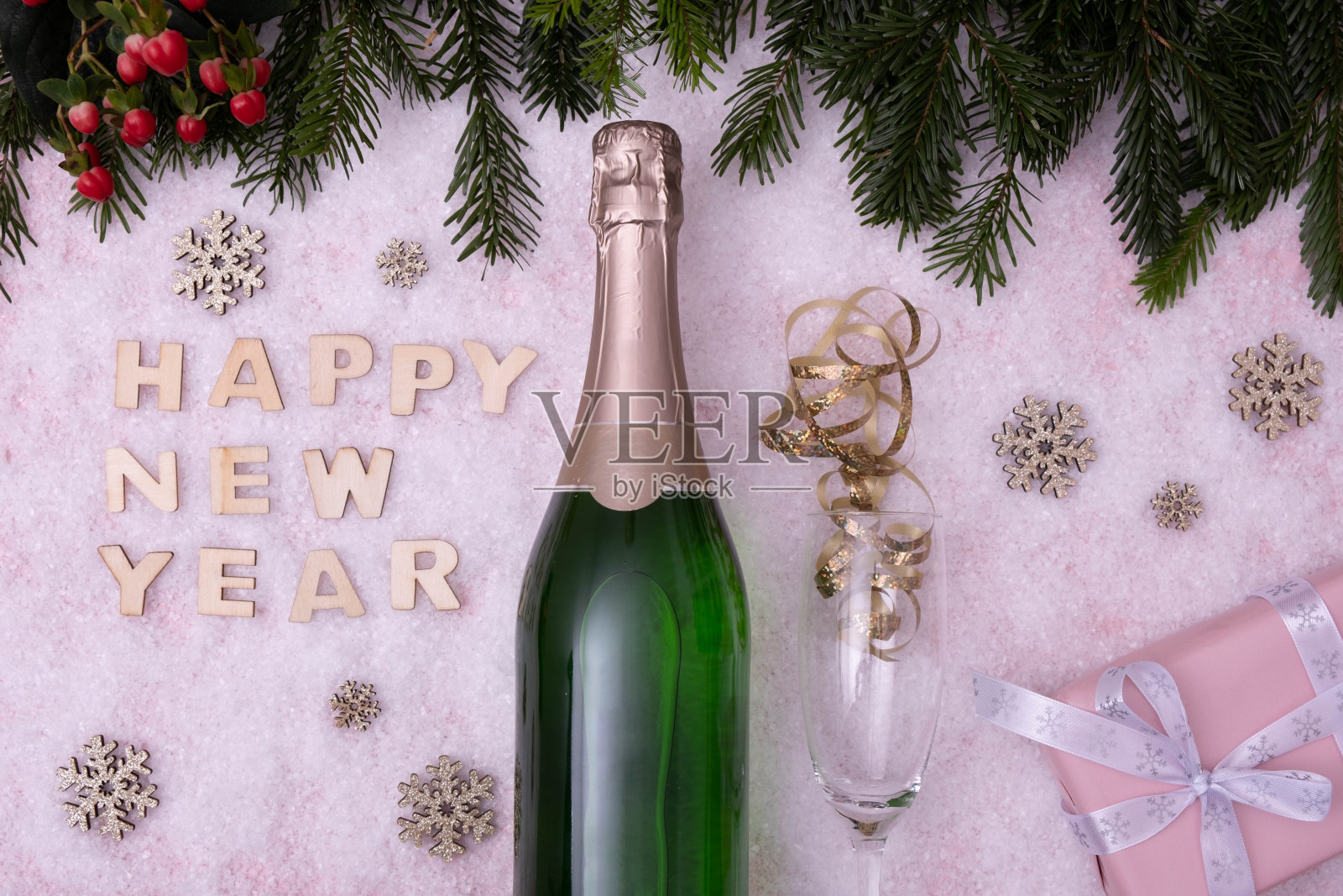 糖果、一瓶香槟、一只玻璃杯、云杉树枝，白色背景上白雪覆盖的桌子上写着“新年快乐”照片摄影图片