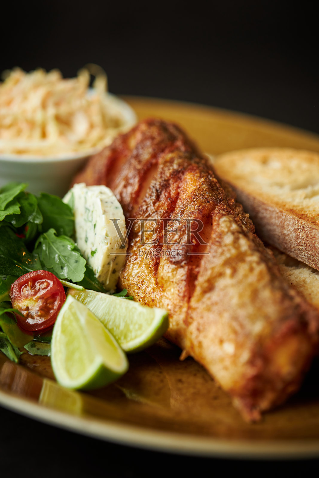 酸橙炸鱼，香草黄油，和沙拉在棕色的盘子照片摄影图片