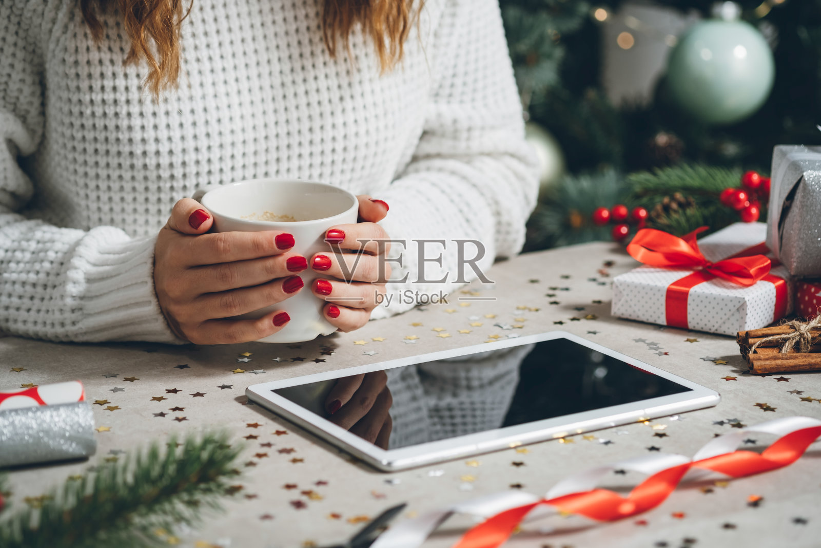 圣诞节前夕，一个陌生的女人拿着咖啡杯，看着平板电脑照片摄影图片
