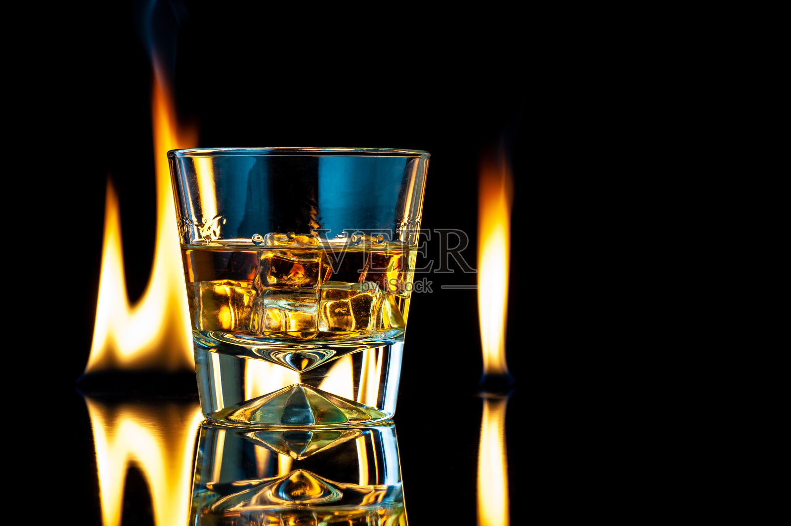 威士忌或波旁威士忌在一个透明的玻璃杯与冰块在一个黑色的背景火。照片摄影图片
