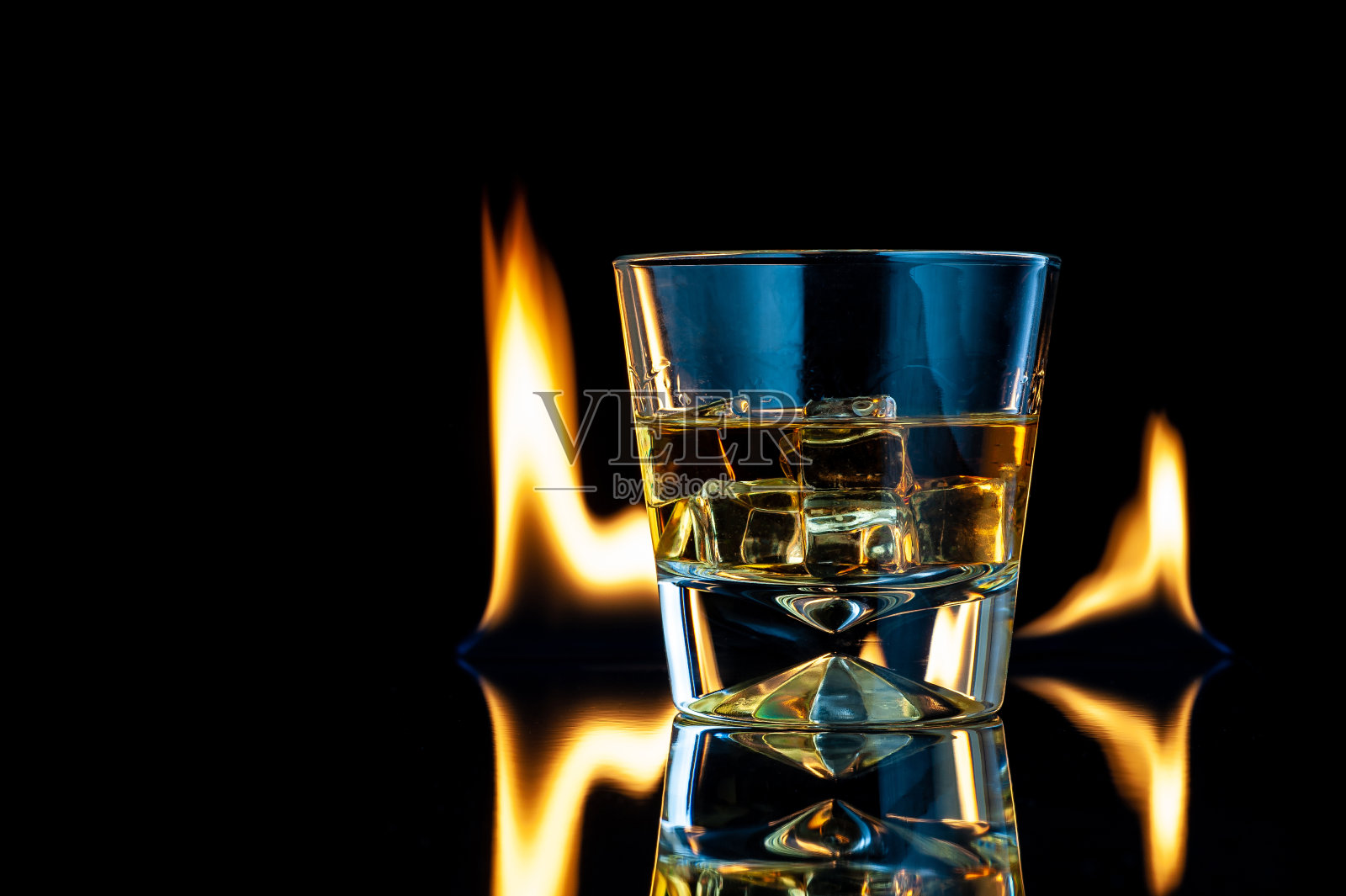 威士忌或波旁威士忌在一个透明的玻璃杯与冰块在一个黑色的背景火。照片摄影图片