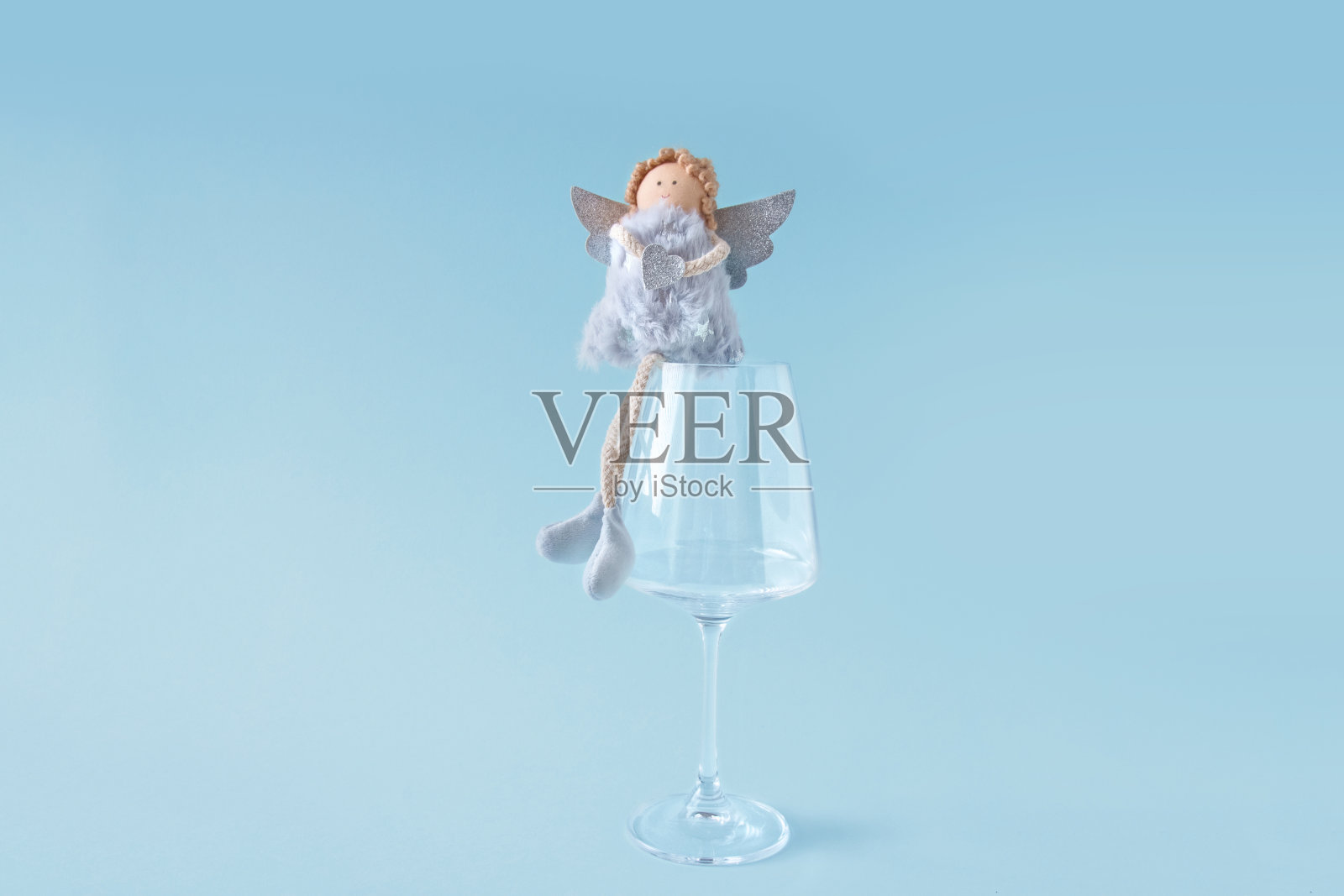 简约的圣诞组成。软天使坐在蓝色背景的大透明酒杯上。照片摄影图片