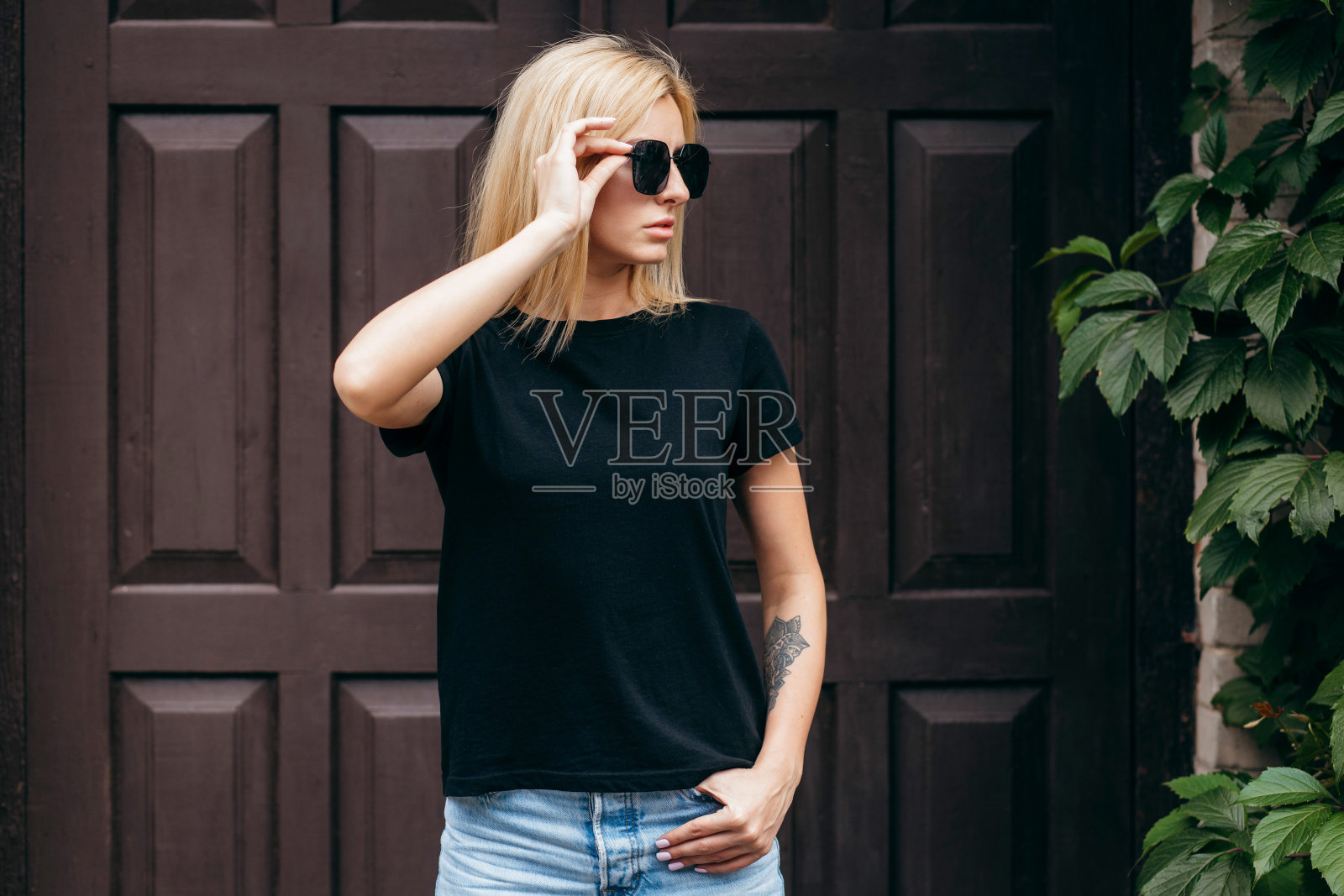 时髦的金发女孩穿着黑色的t恤和眼镜摆姿势，对着街道，城市的服装风格。照片摄影图片