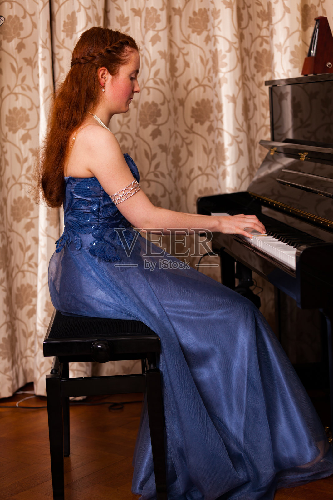 一个穿着古典蓝色衣服的女孩在一个靠窗帘的家庭背景下弹钢琴照片摄影图片