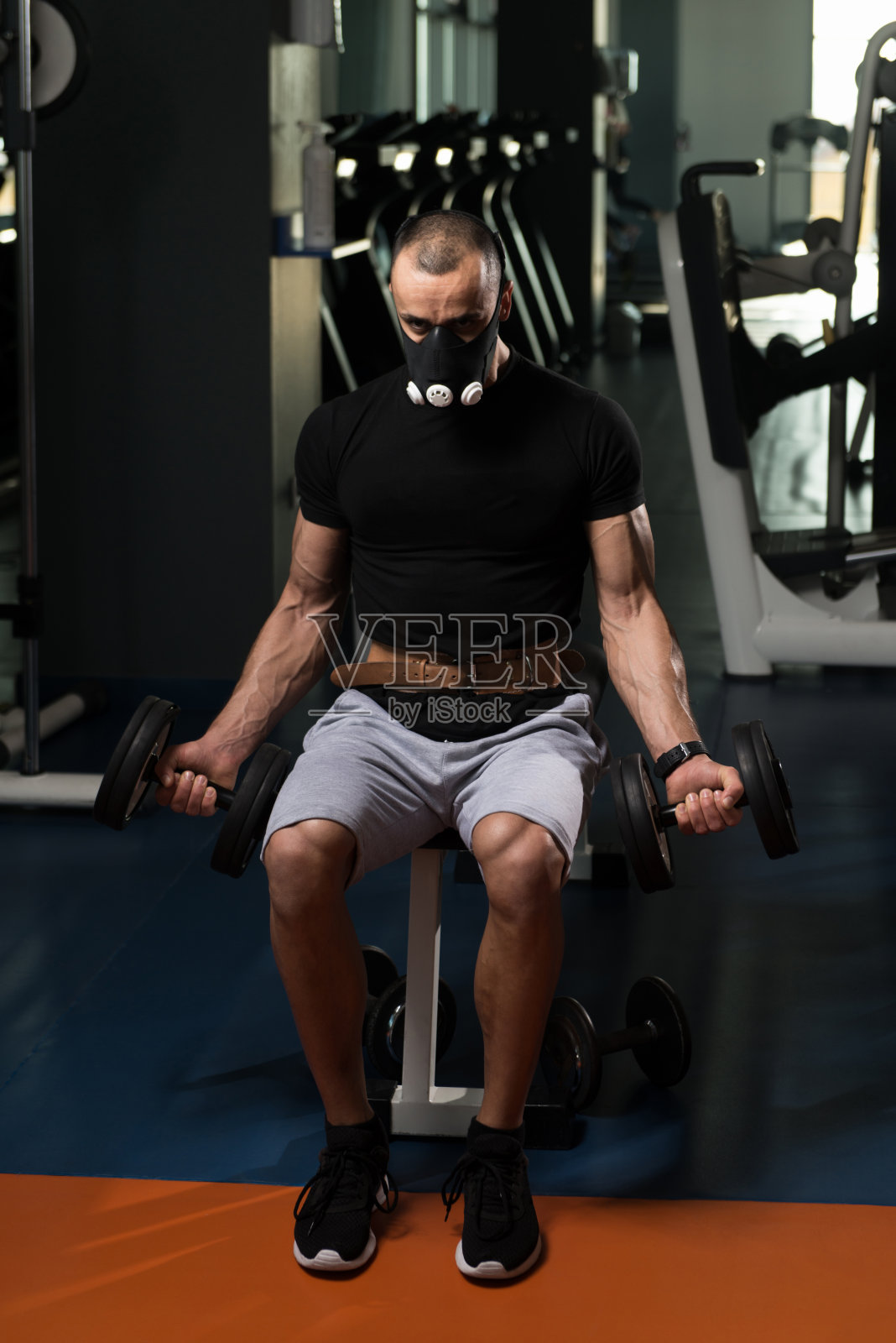 健美运动员锻炼二头肌与哑铃在海拔面具照片摄影图片