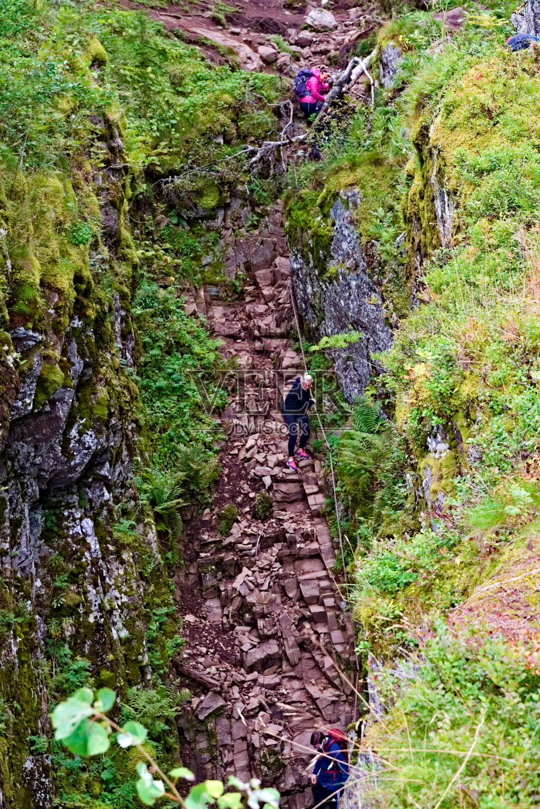 用岩石和绳索爬过陡峭峡谷的徒步旅行者。照片摄影图片