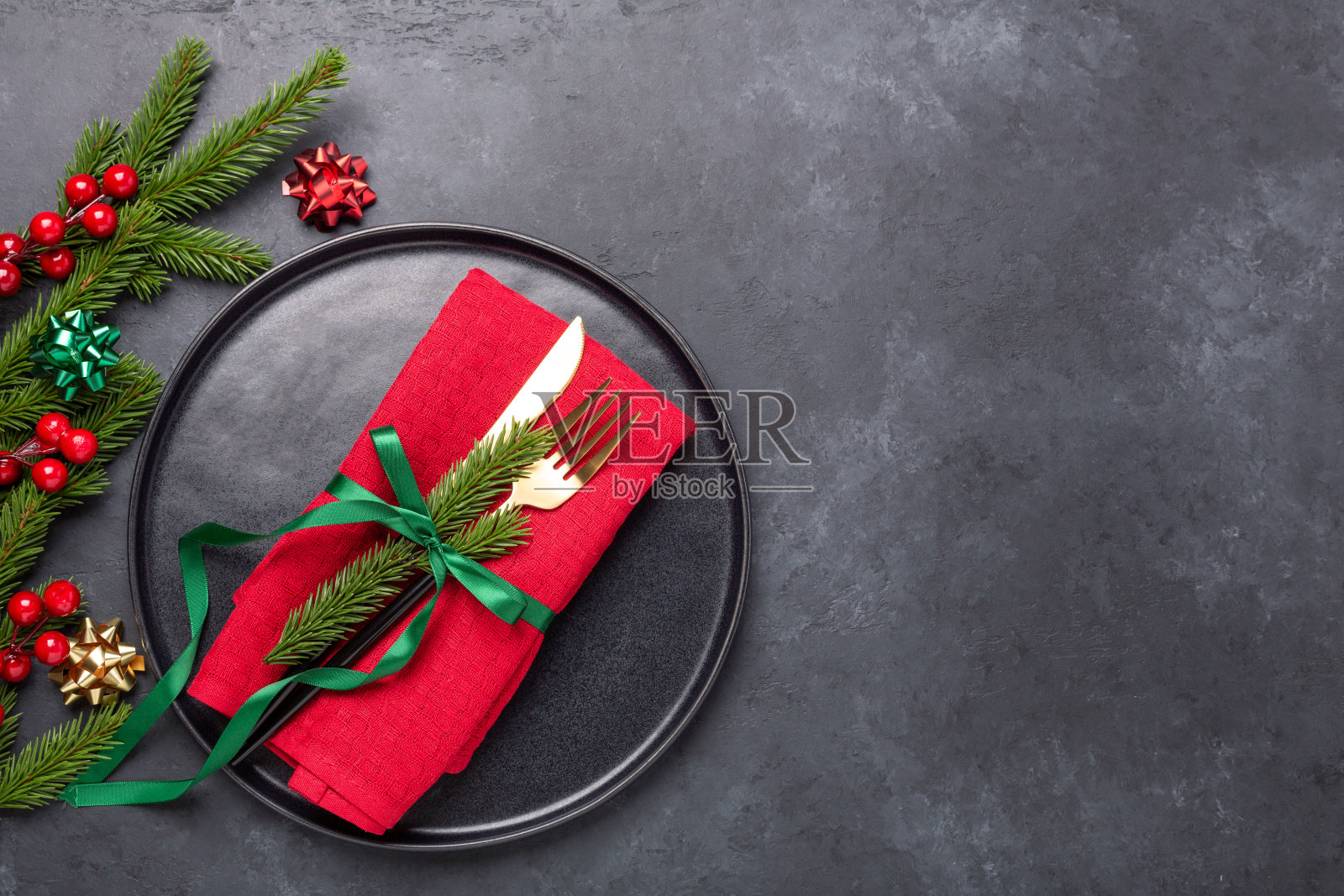 圣诞餐桌设置黑色陶瓷板，杉木树枝和金色和红色的配件在黑色的石头背景。前视图。本空间照片摄影图片