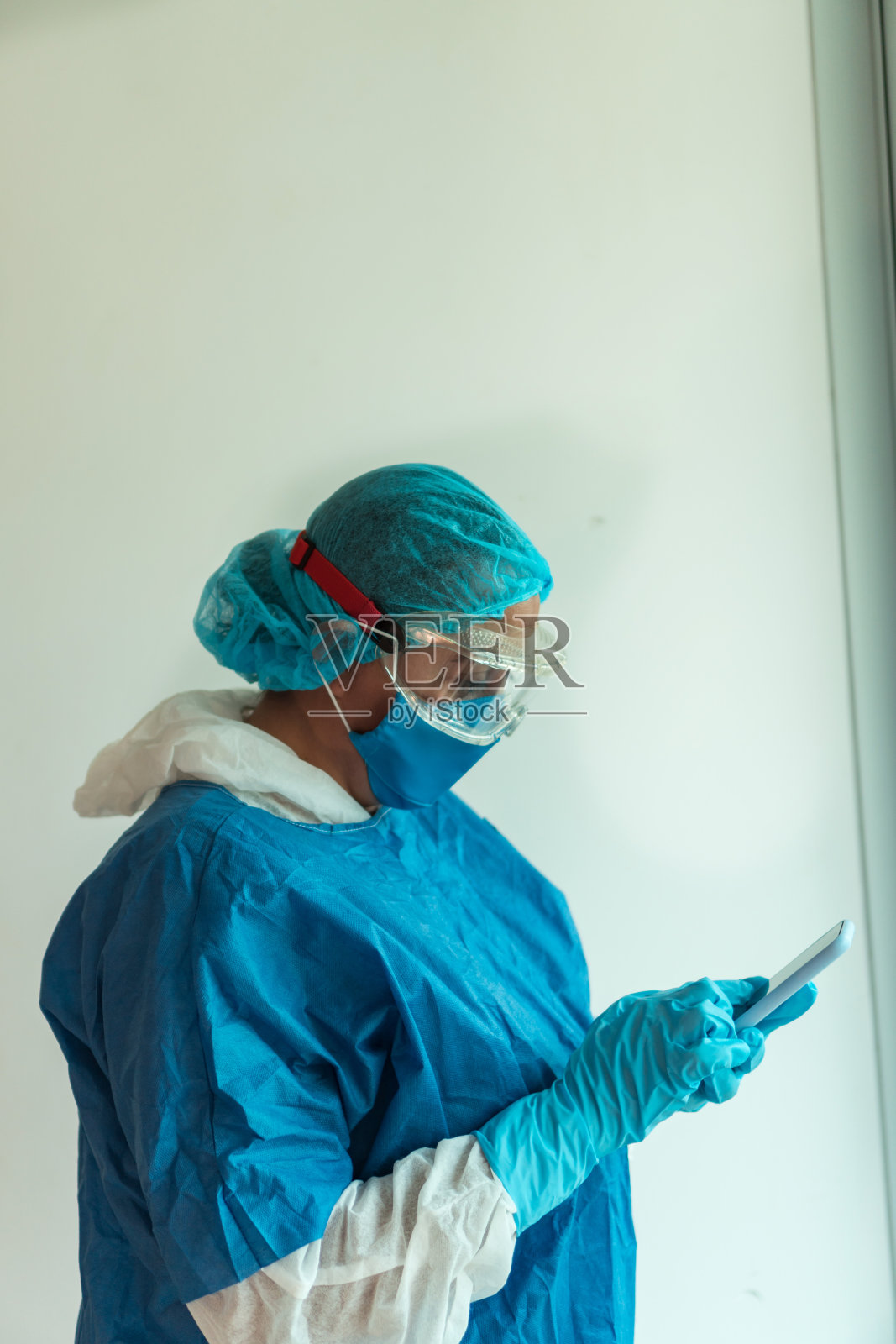 年轻，严肃的医生穿着蓝色制服和医用口罩在一个诊所工作手机和乳胶手套照片摄影图片