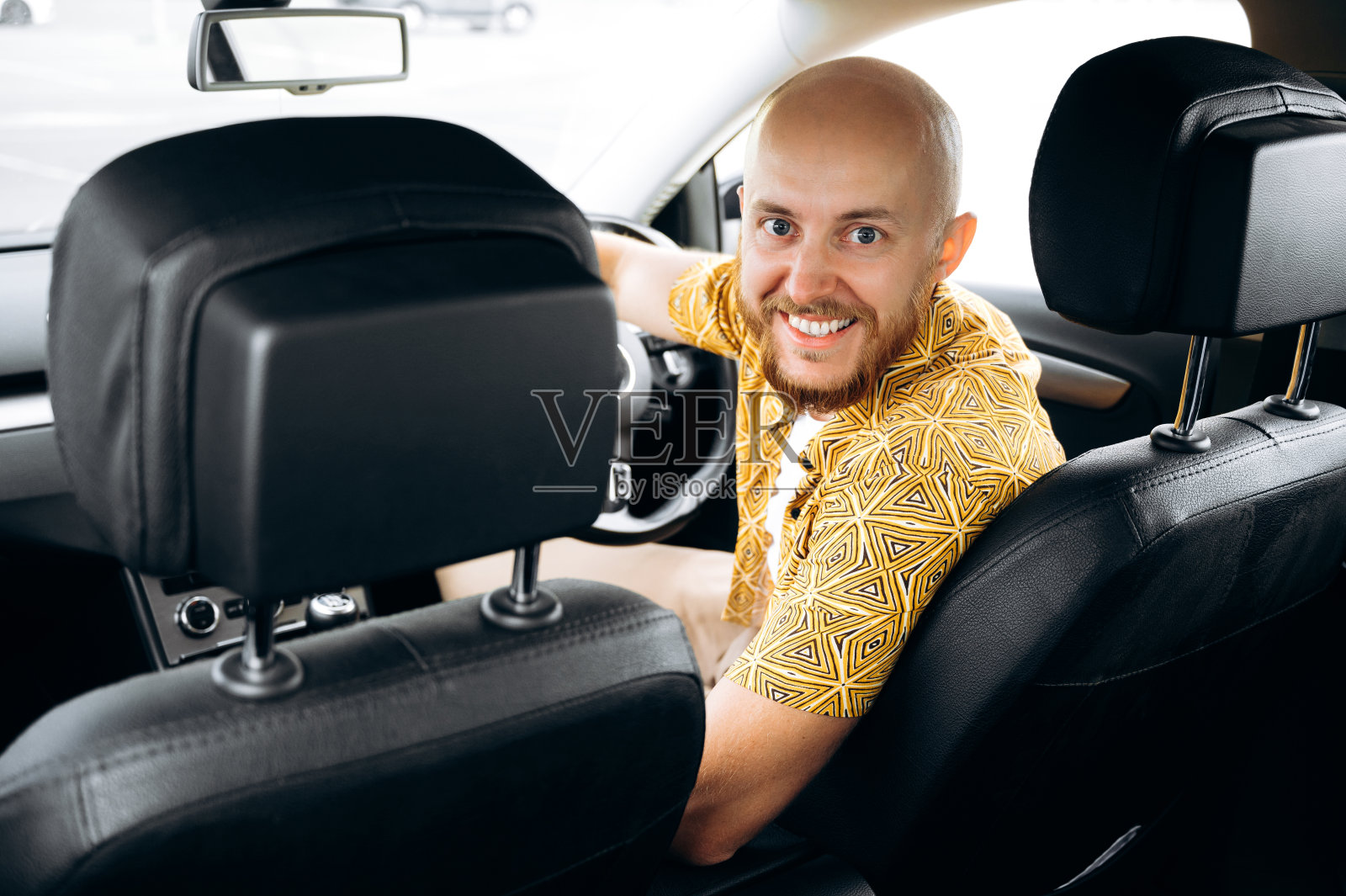 积极的大胡子司机。微笑的男人穿着休闲服坐在他的车的方向盘后面看着相机和微笑照片摄影图片
