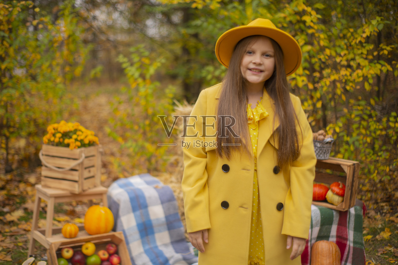 可爱美丽的十几岁的黑发女孩，戴着橙色的帽子，穿着和外套旁边的秋季装饰品-南瓜，苹果，毯子，干草。舒适照片摄影图片