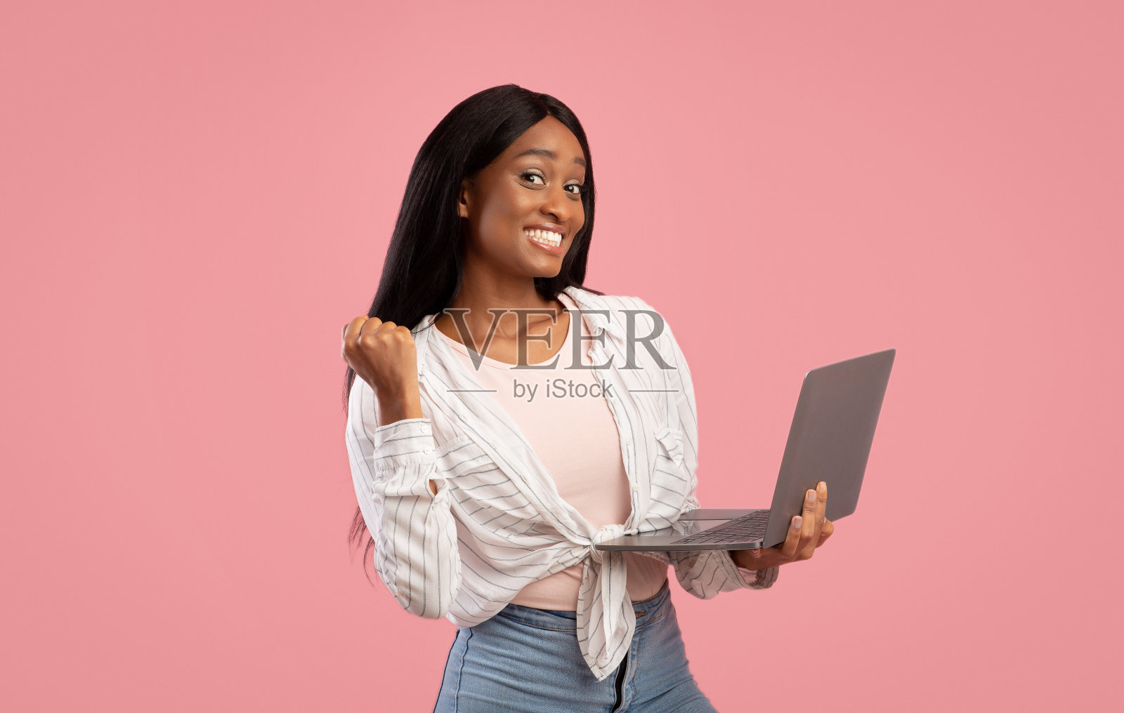 千禧一代非洲裔美国女士用笔记本电脑做YES手势，并在粉红色的工作室背景上微笑照片摄影图片