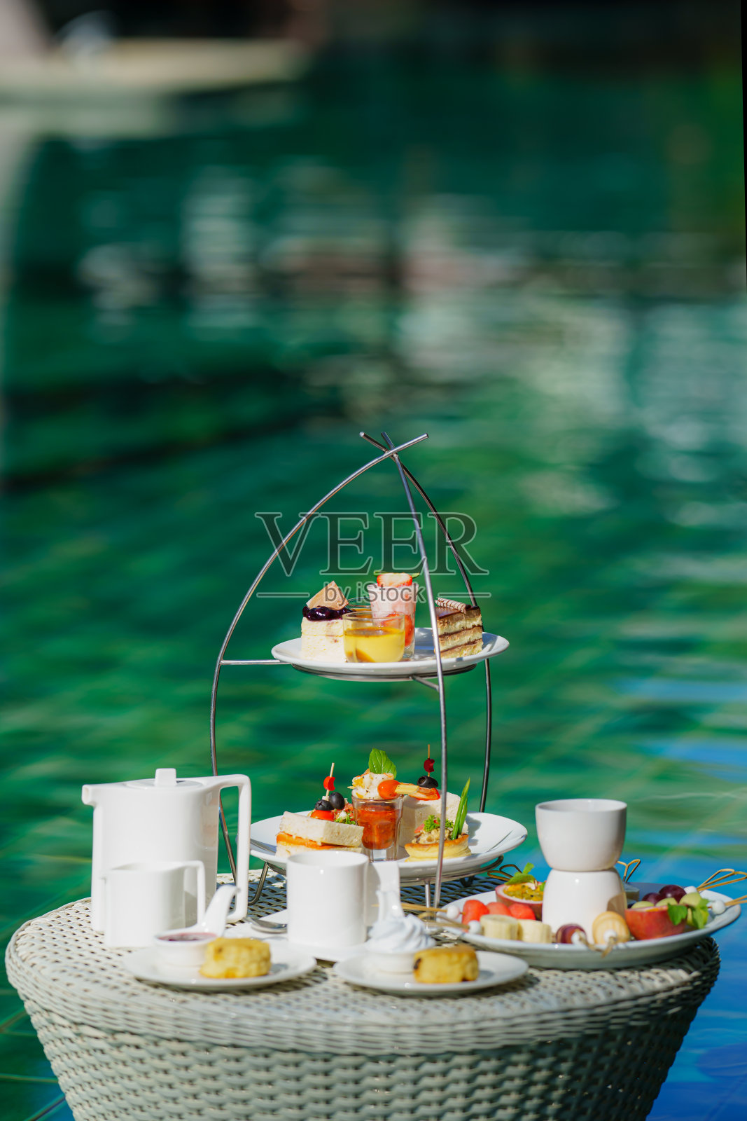 一套下午茶或咖啡，搭配各种蛋糕、饼干和水果，以度假村泳池边为背景照片摄影图片