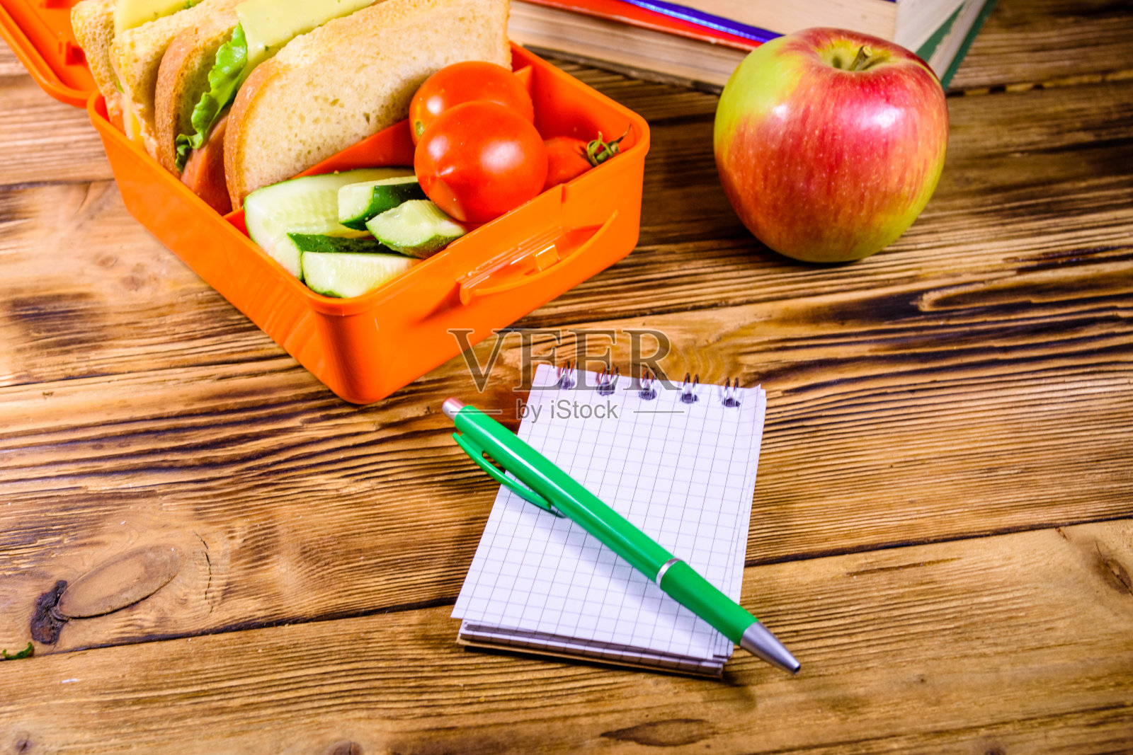 笔记本，笔，成熟的苹果，一堆书和午餐盒三明治，黄瓜和西红柿在木桌上照片摄影图片