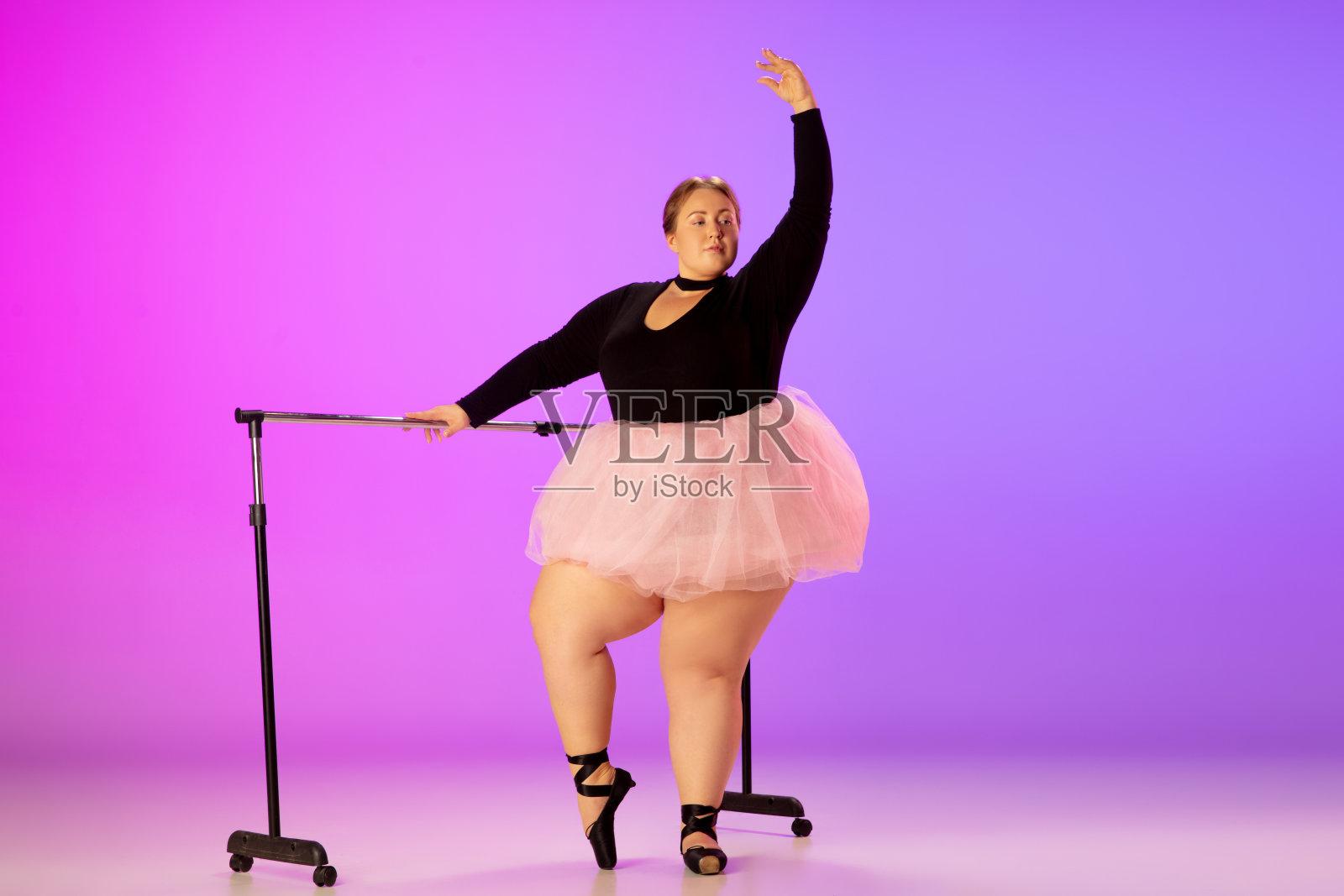 美丽的高加索大尺寸模特练习芭蕾舞蹈在梯度紫色粉红色的工作室背景在霓虹灯照片摄影图片