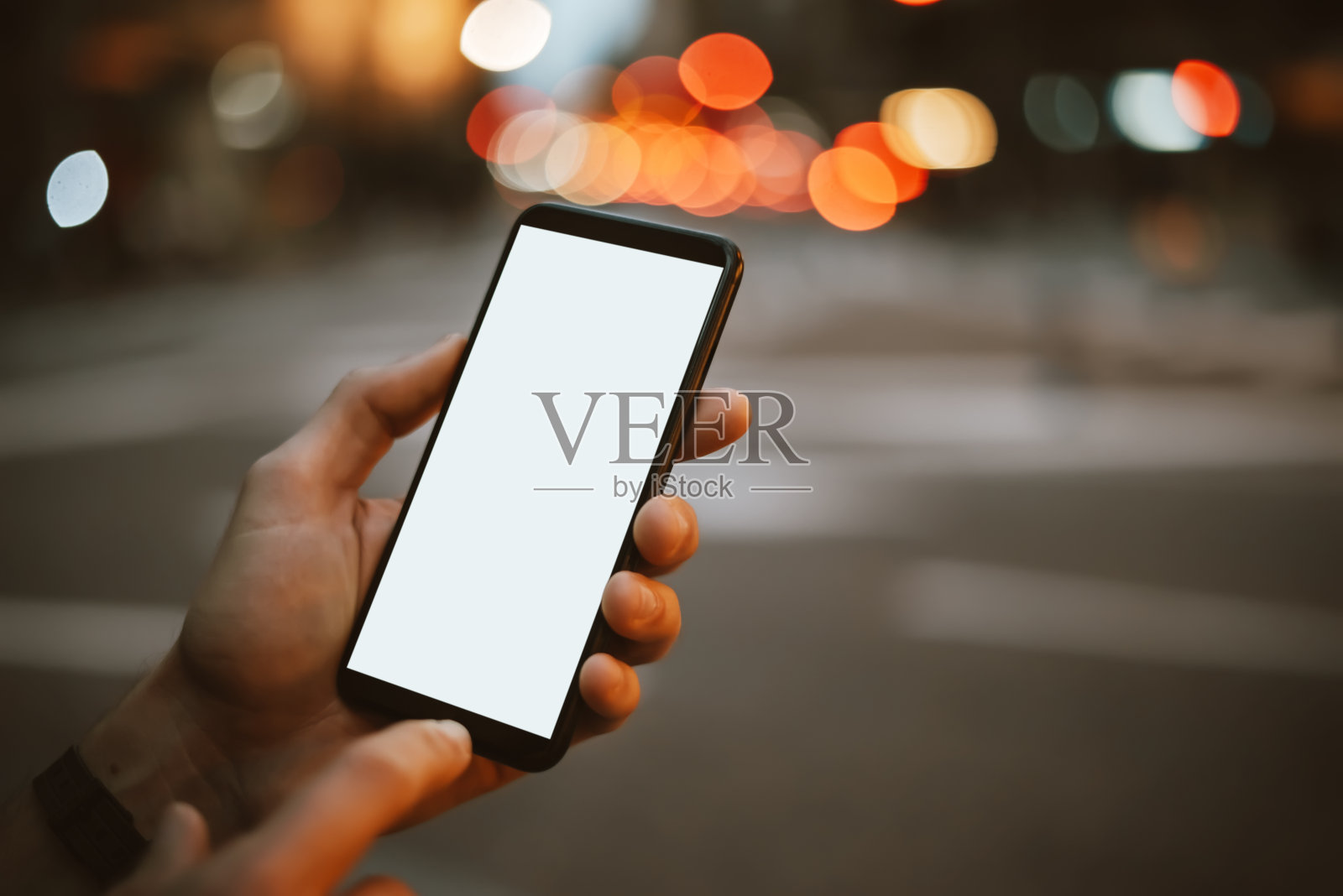 在夜晚的街道上，男性用智能手机的手的特写。空空白屏幕。模型照片摄影图片
