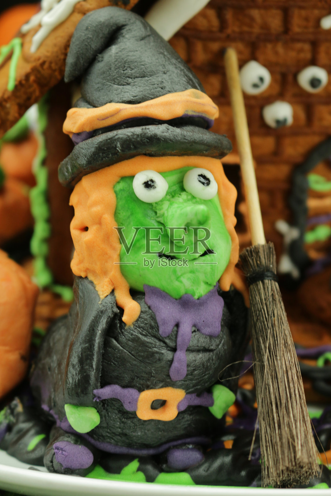 这是自制的万圣节姜饼饼干屋的特写图片，在苔藓的工作台上用糖霜和糖果糖果装饰，南瓜和女巫雕像照片摄影图片