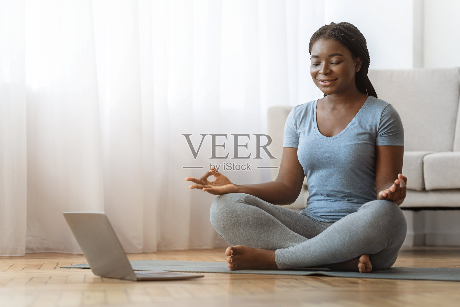 和平的非洲女士在家里的笔记本电脑前冥想，练习瑜伽照片摄影图片