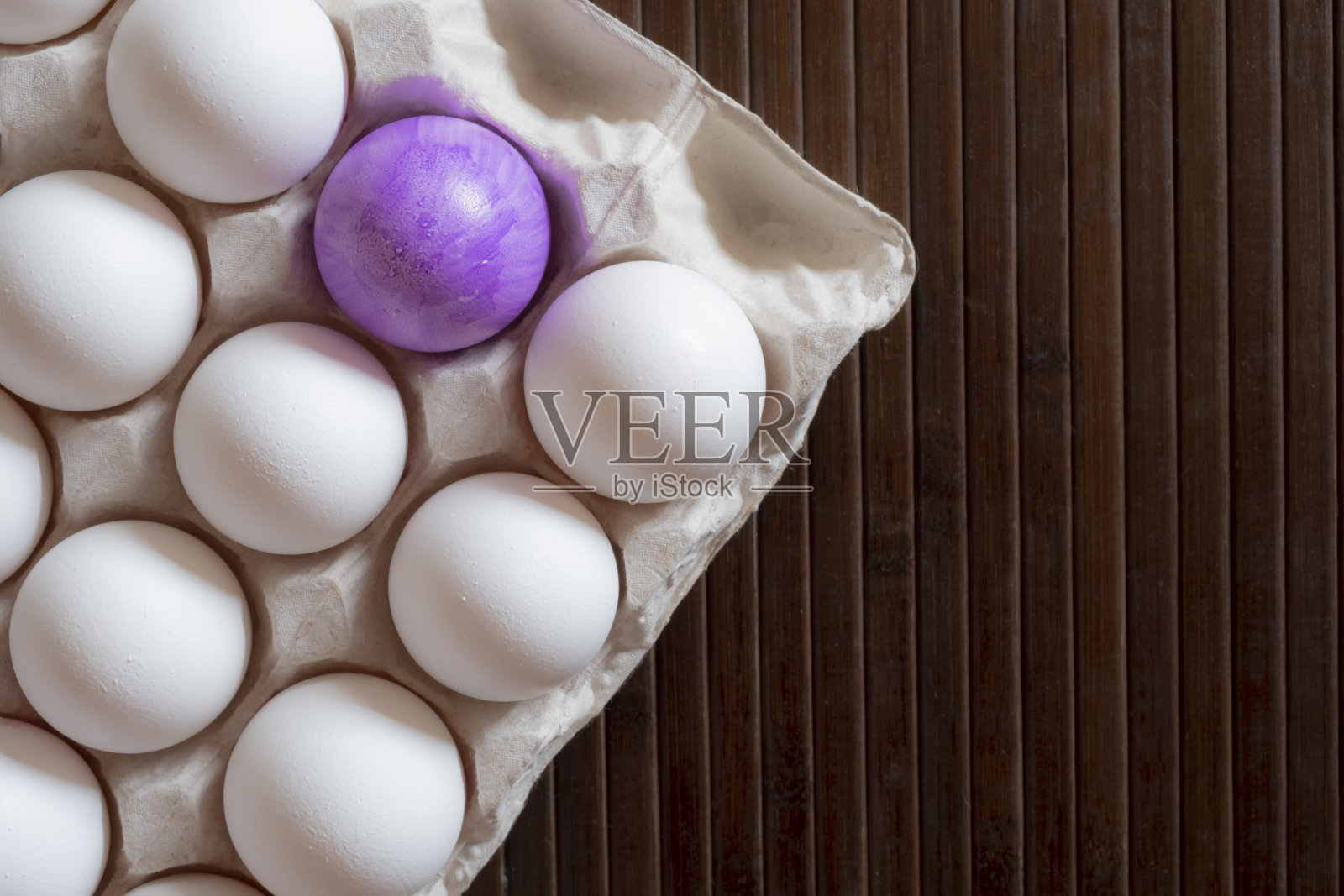 白色的鸡蛋放在一个纸板箱里，背景是一个彩绘的鸡蛋。复活节彩蛋。白色的鸡蛋中有彩蛋。照片摄影图片
