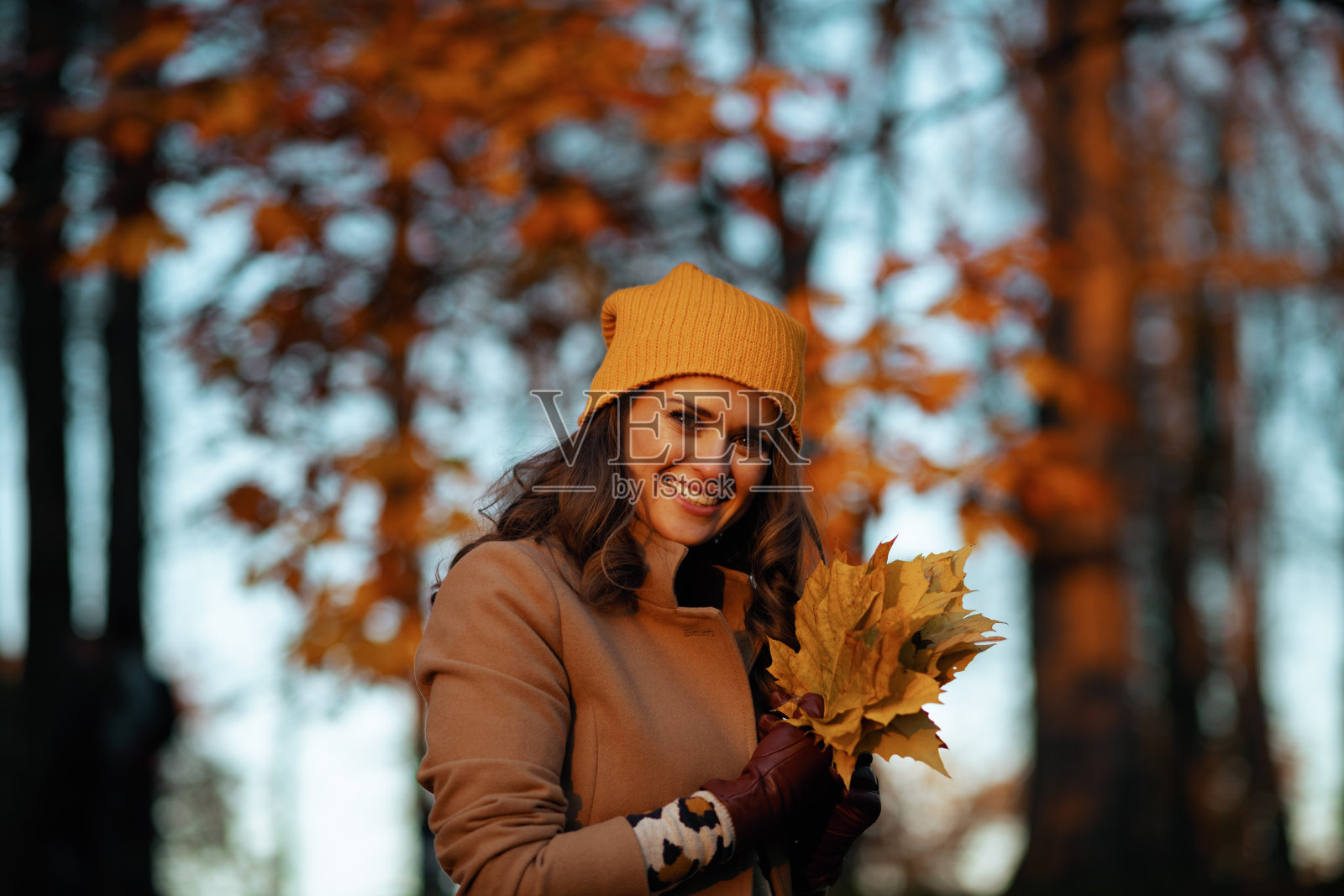 穿着棕色大衣，戴着黄色帽子的漂亮女人微笑着照片摄影图片