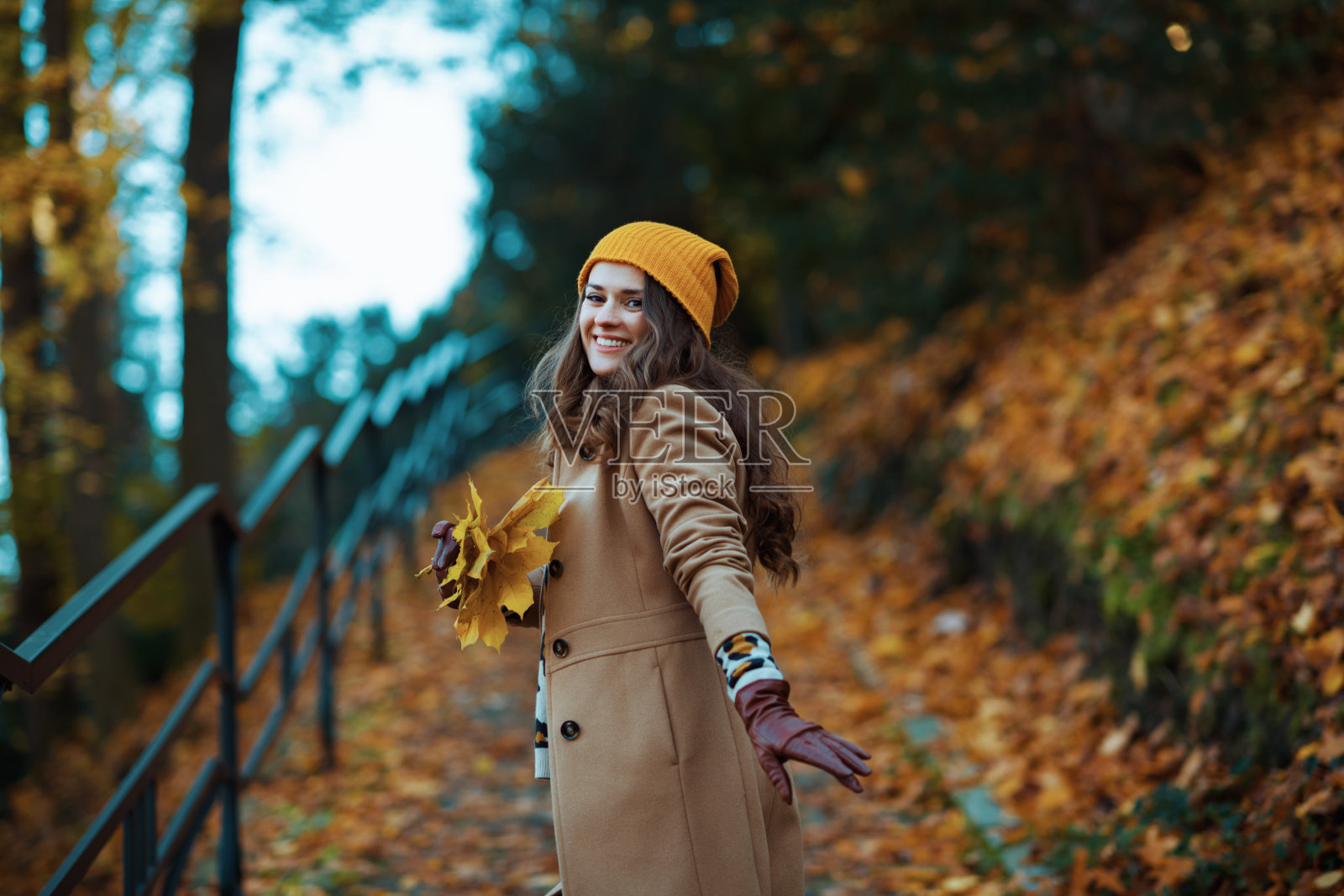 穿着棕色大衣，戴着帽子的快乐女人正在散步照片摄影图片