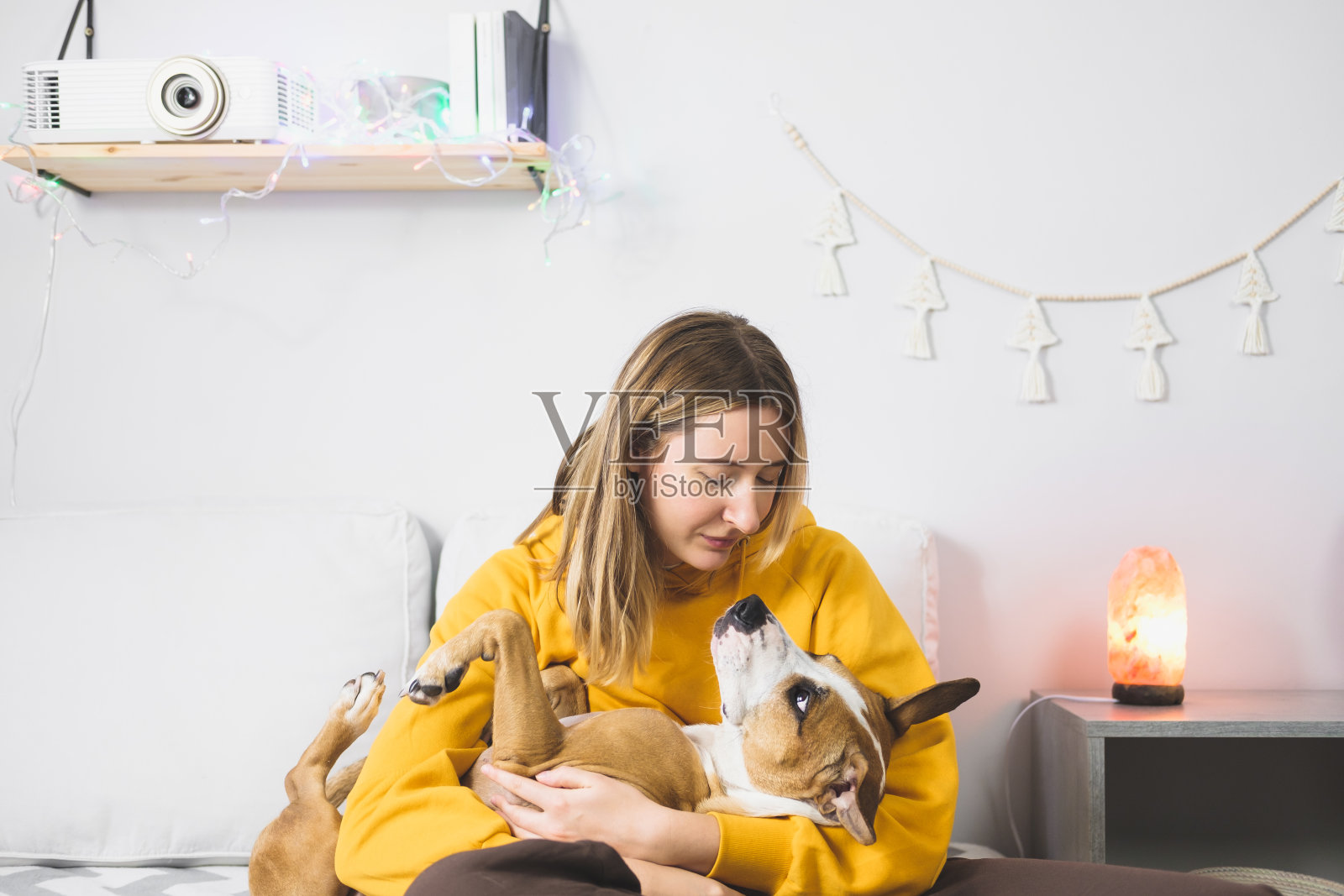 年轻女子拥抱她的狗，室内卧室场景。照片摄影图片