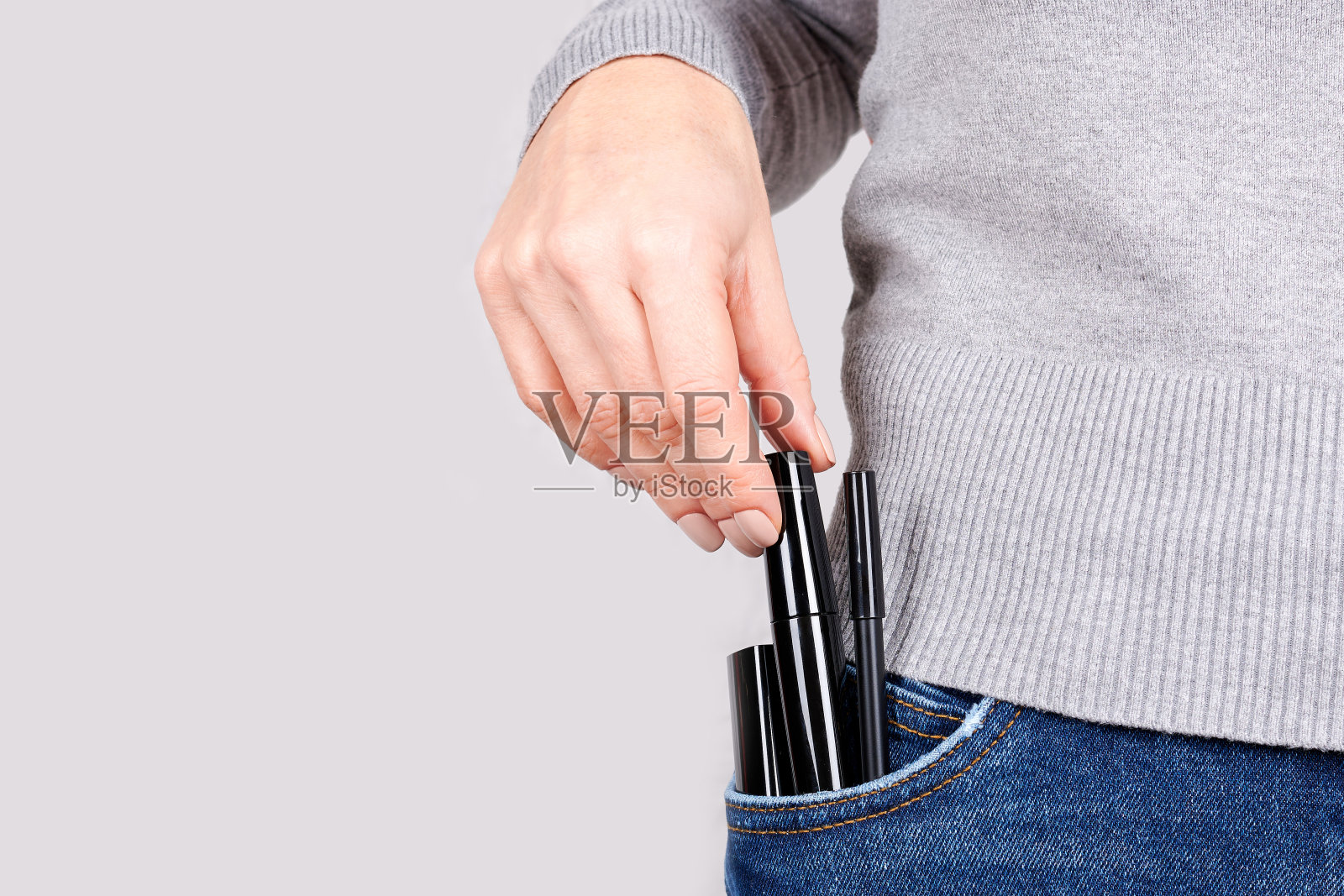 在灰色背景下，将化妆物品放在牛仔裤口袋里。照片摄影图片