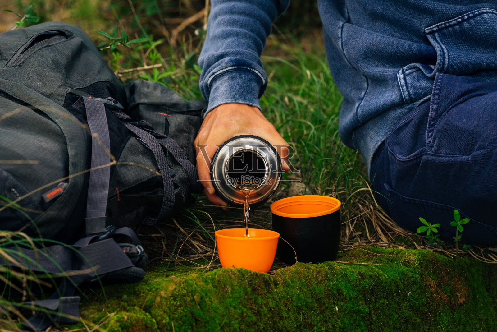 徒步旅行时喝热水瓶里的茶。男人用手从热水瓶里倒热茶照片摄影图片
