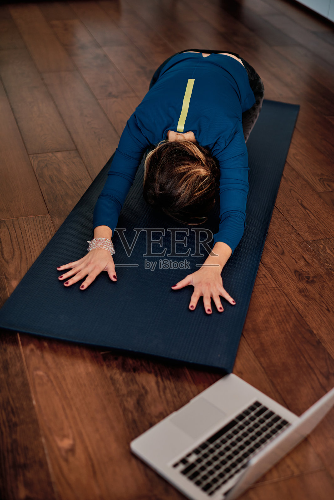 中年妇女在家里的儿童瑜伽姿势后，在笔记本电脑上在线讲座。照片摄影图片