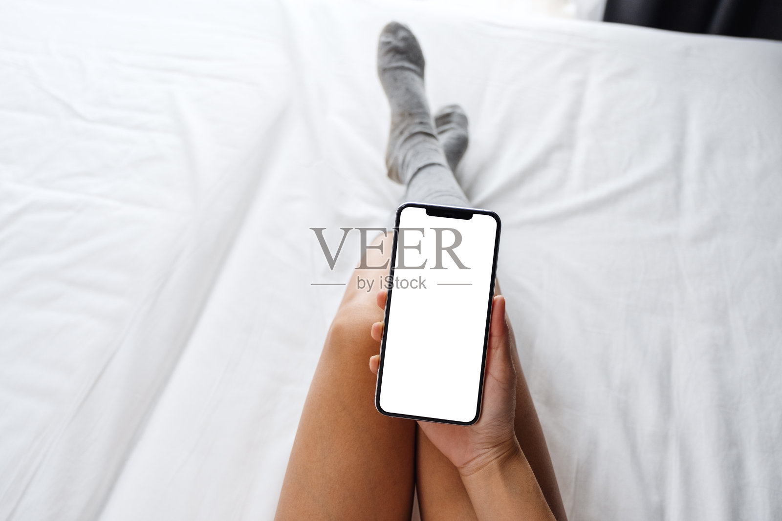 一名女子躺在舒适的白色床上，手里拿着白色手机，桌面屏幕是空白的照片摄影图片