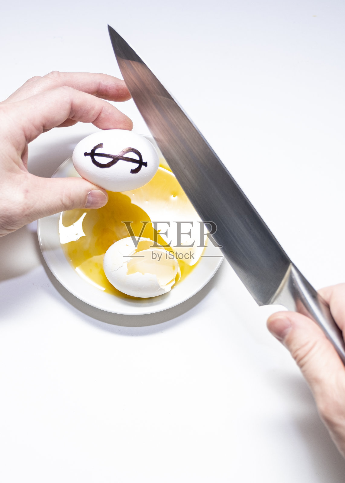 一名身穿西装的白人男子用一把刀打碎了一个带有美元货币符号的鸡蛋。白色盘子里的蛋黄。照片摄影图片