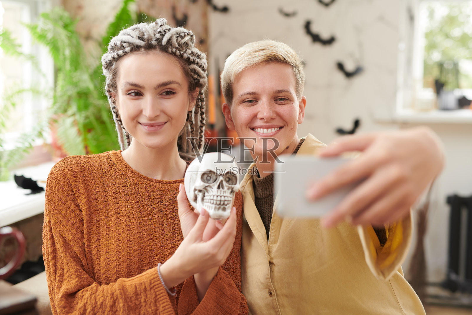 积极的女孩摆着骷髅头在万圣节派对上用智能手机自拍照片摄影图片