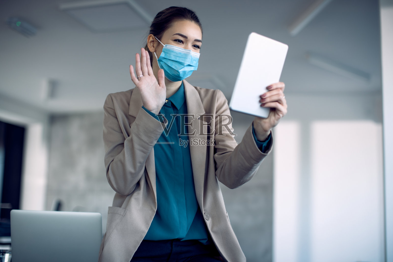 快乐的女商人挥手，同时在她的办公室通过数字平板电脑进行视频通话。照片摄影图片