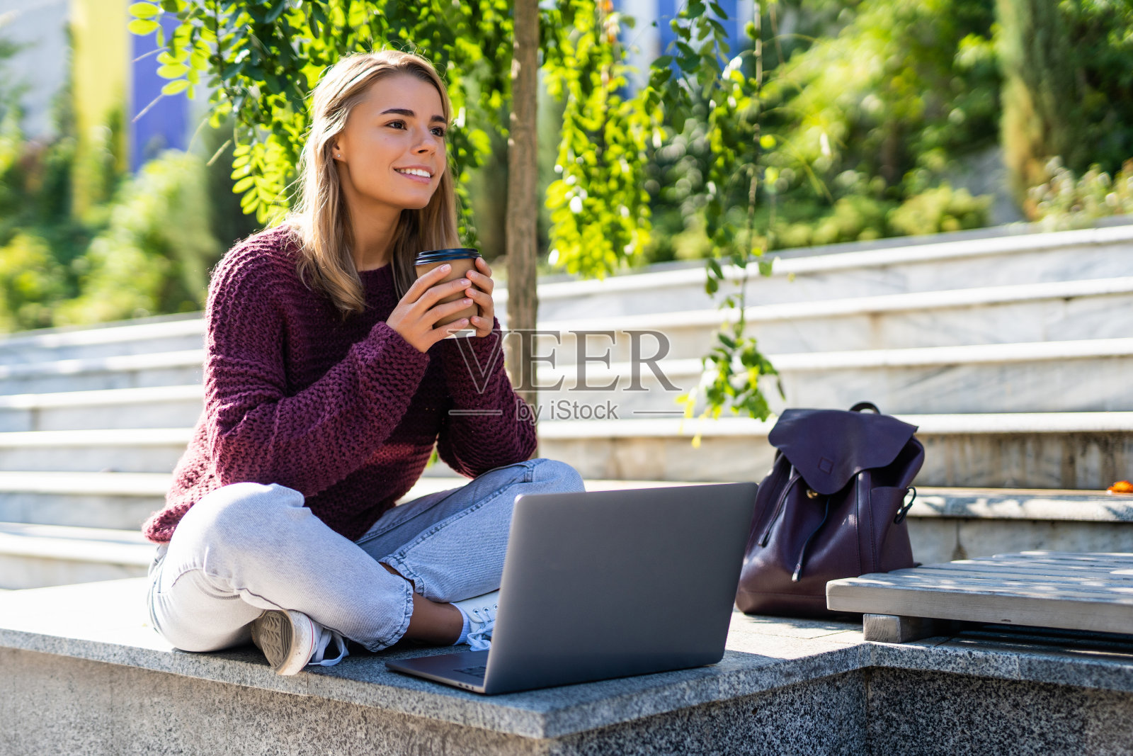 来自世界各地工作。一个快乐美丽的女人坐在户外的长椅上喝咖啡和使用笔记本电脑的肖像照片摄影图片