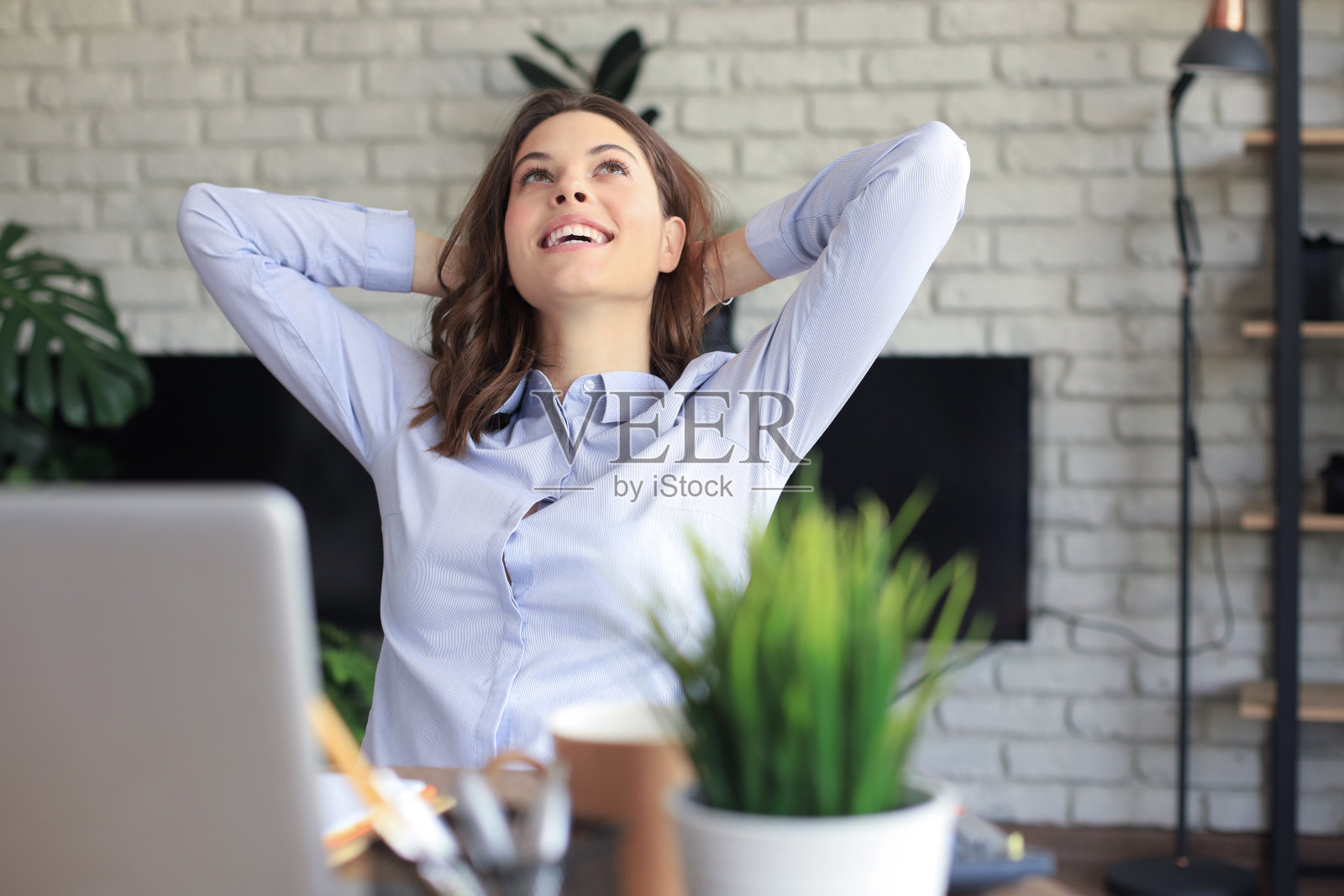 年轻女子双手抱头，在家享受休息时间。安详悠闲的女商人坐在桌子旁，电脑旁，一边看一边梦想着未来。照片摄影图片