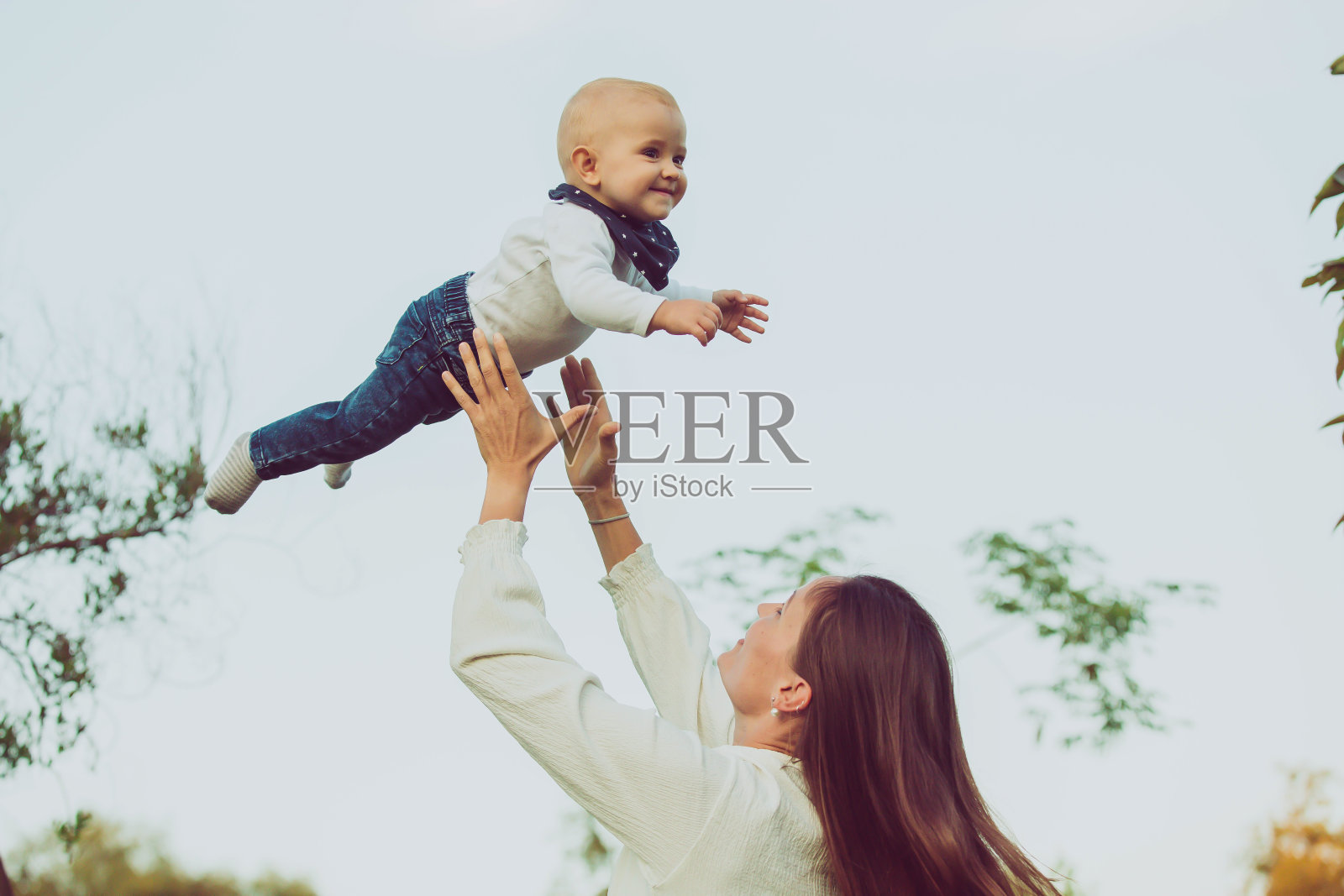 一位迷人的母亲将一个可爱的婴儿轻轻抛向空中。照片摄影图片