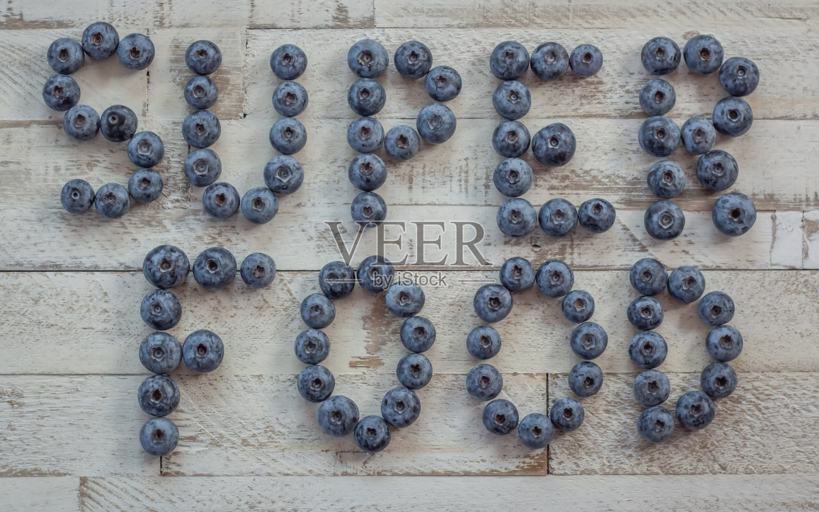 “超级食物”这个词用蓝莓写在一个白色的复古木制背景上照片摄影图片