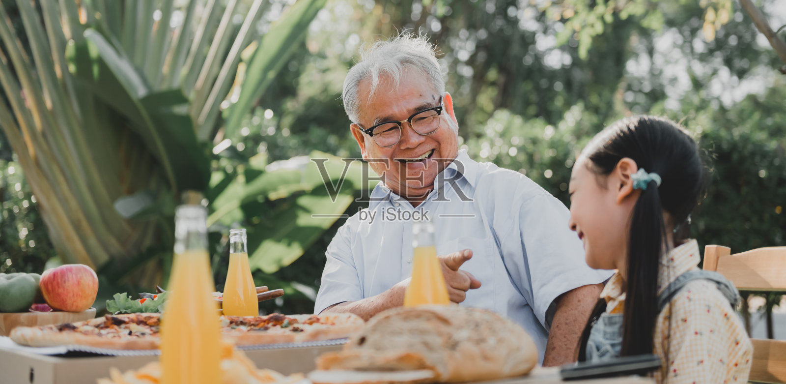 爷爷和孙女在家花园里吃披萨。退休年龄的生活方式与家人在暑假。照片摄影图片
